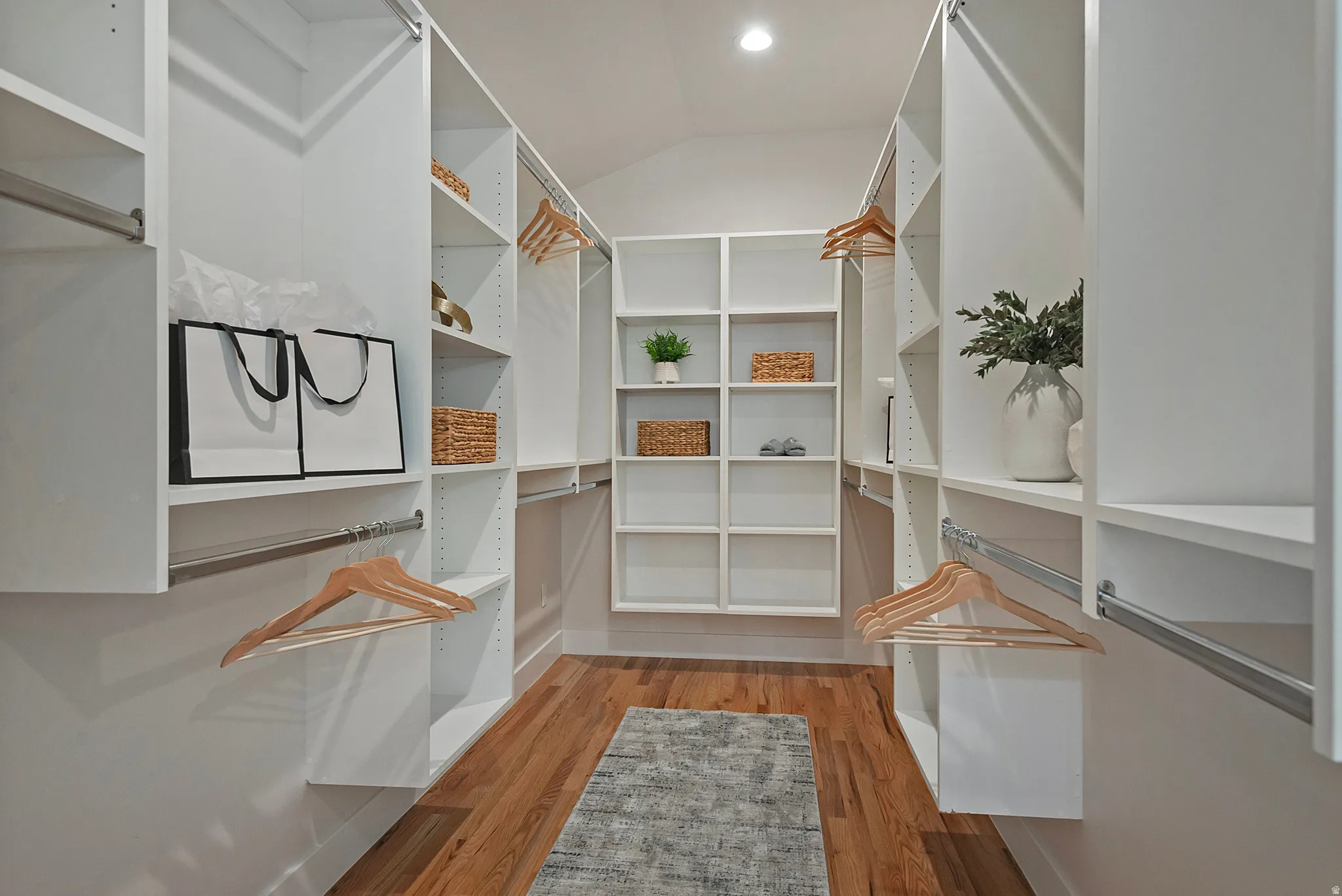 Huge primary walk in closet with light wood finished floors and vaulted ceiling