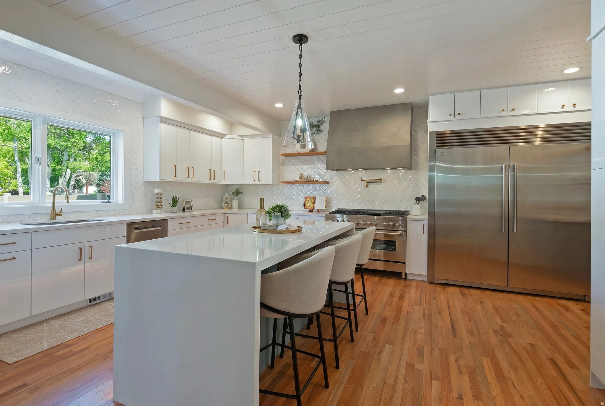 Kitchen with premium appliances, pendant lighting, upgraded cabinetry, a breakfast bar area, and light wood finished floors