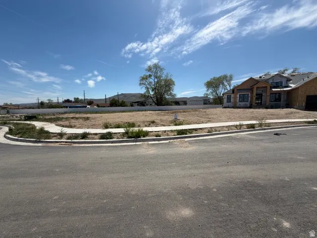 Cleared lot with newly paved street frontage, concrete sidewalk, and a partially constructed residence to the right