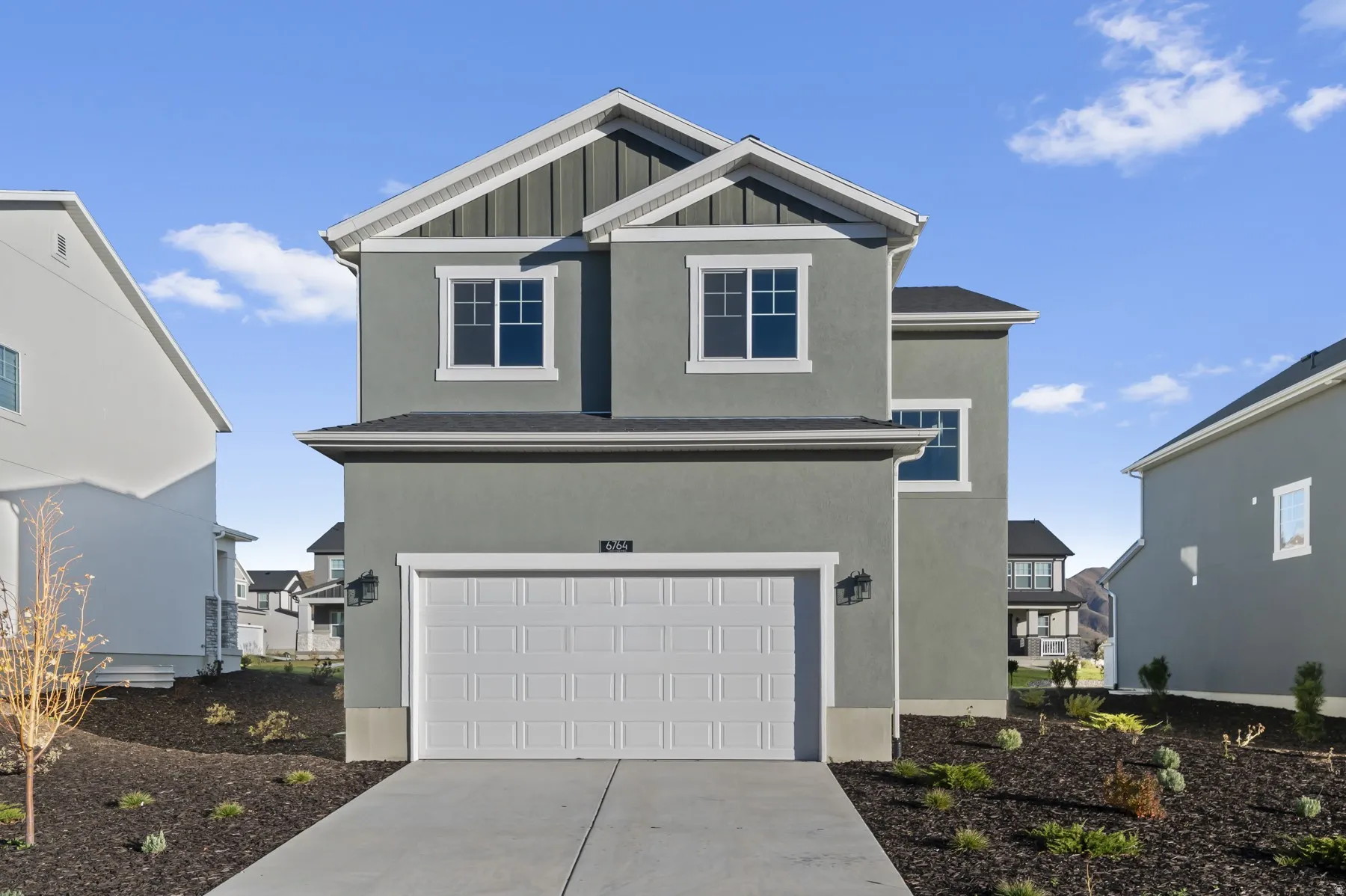 Contemporary two-story residence with a stucco and board-and-batten facade, featuring white trim and a prominent two-car garage