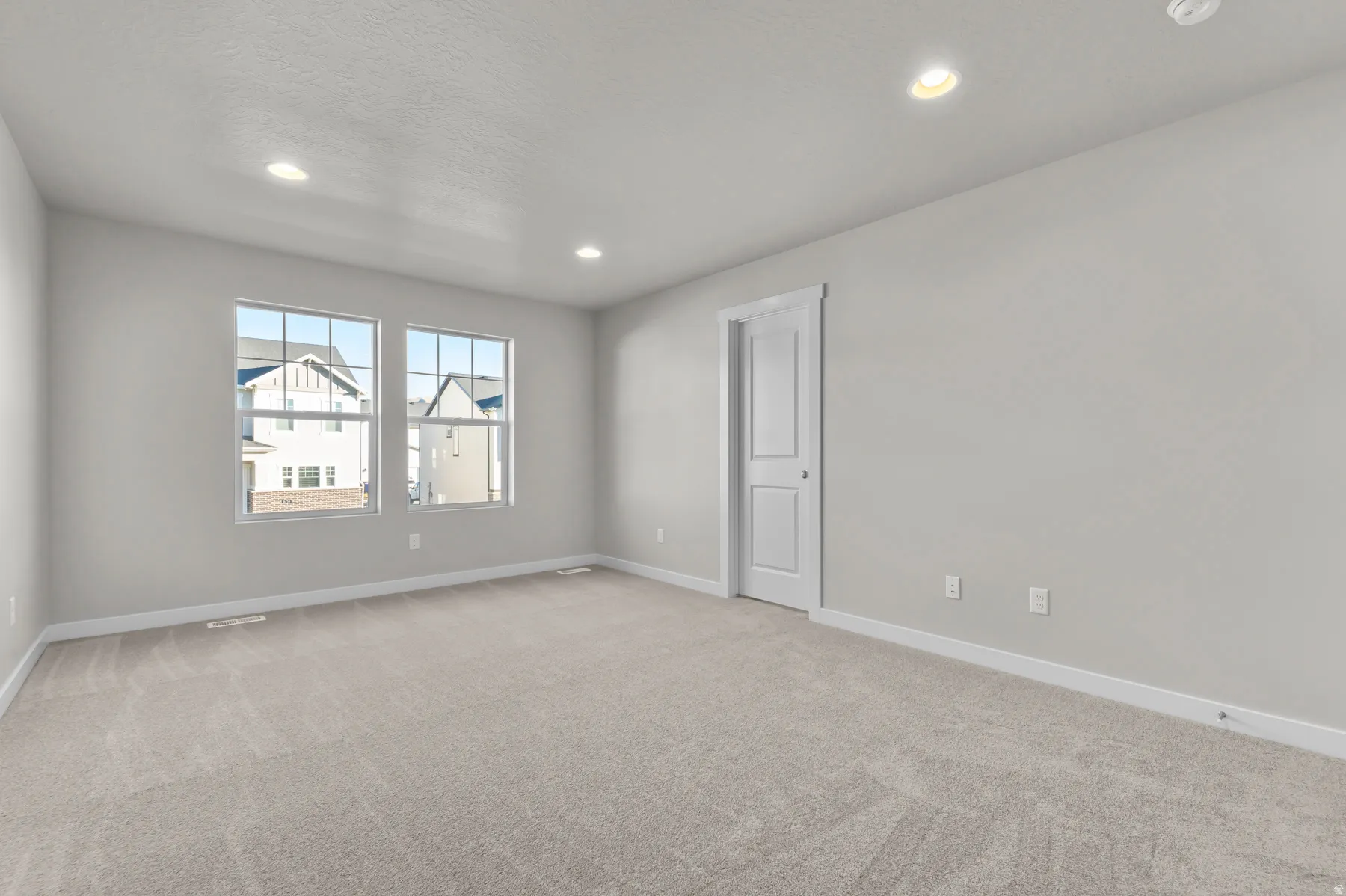 Spacious room featuring light gray walls, plush gray carpet flooring, and white baseboards