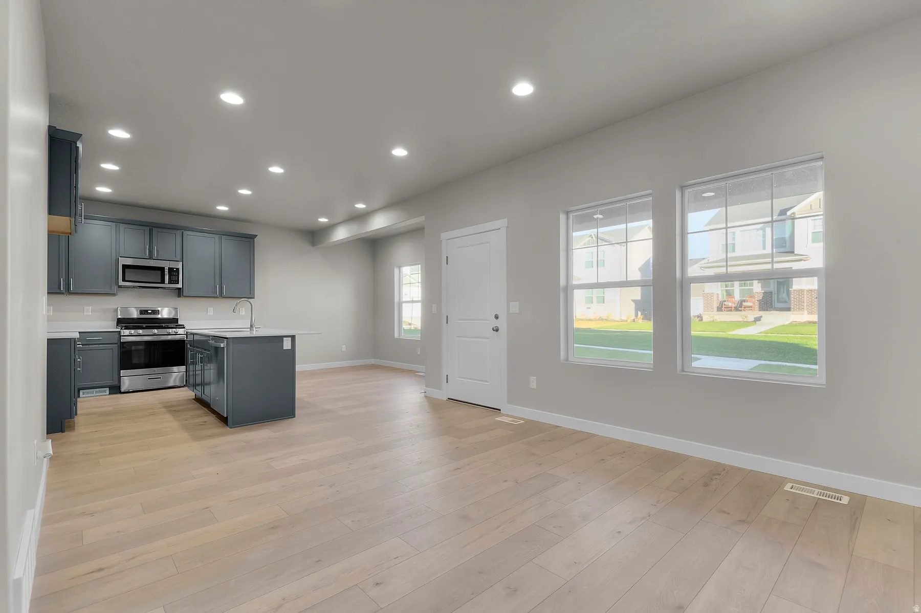 Open-concept living space with light wood-finish flooring, recessed ceiling lighting, and multiple windows