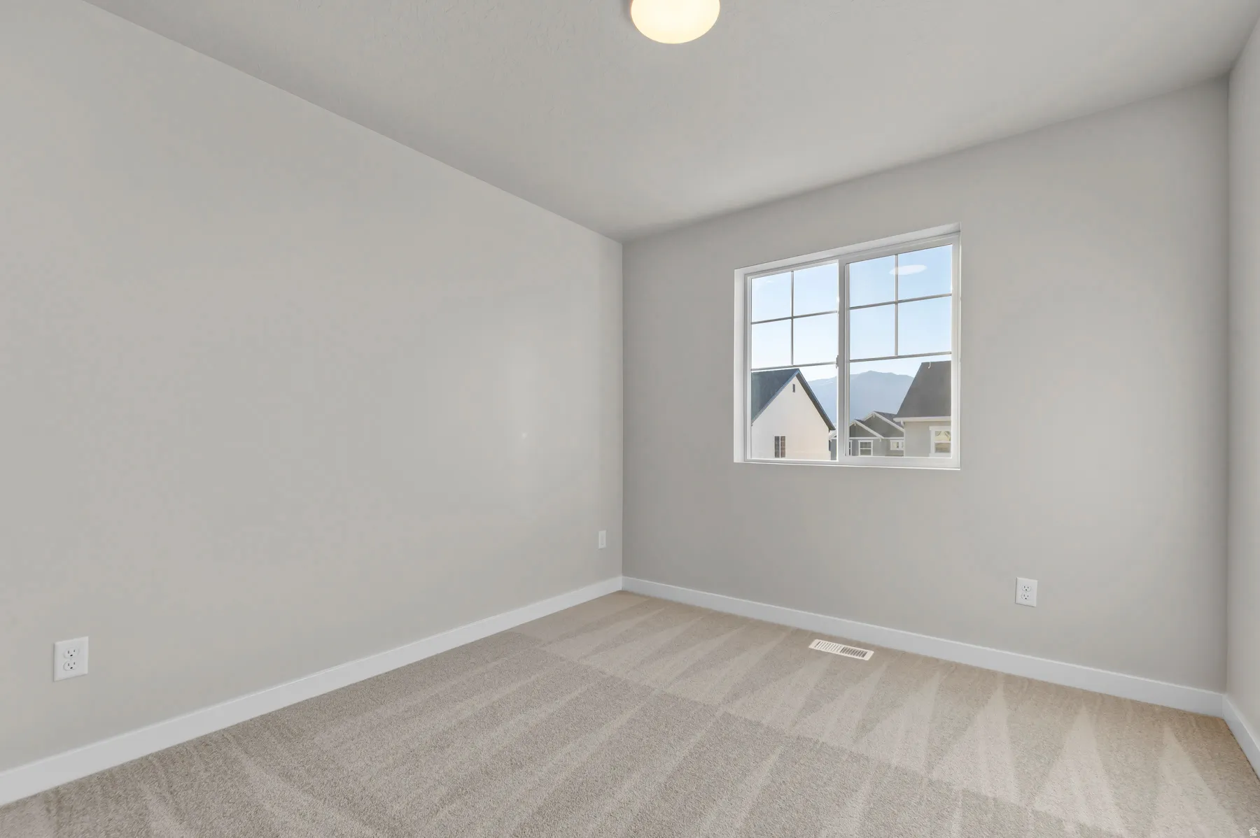Neutral-toned room featuring a large window with grid panes, textured carpet flooring, white baseboards, and a flush mount ceiling light fixture