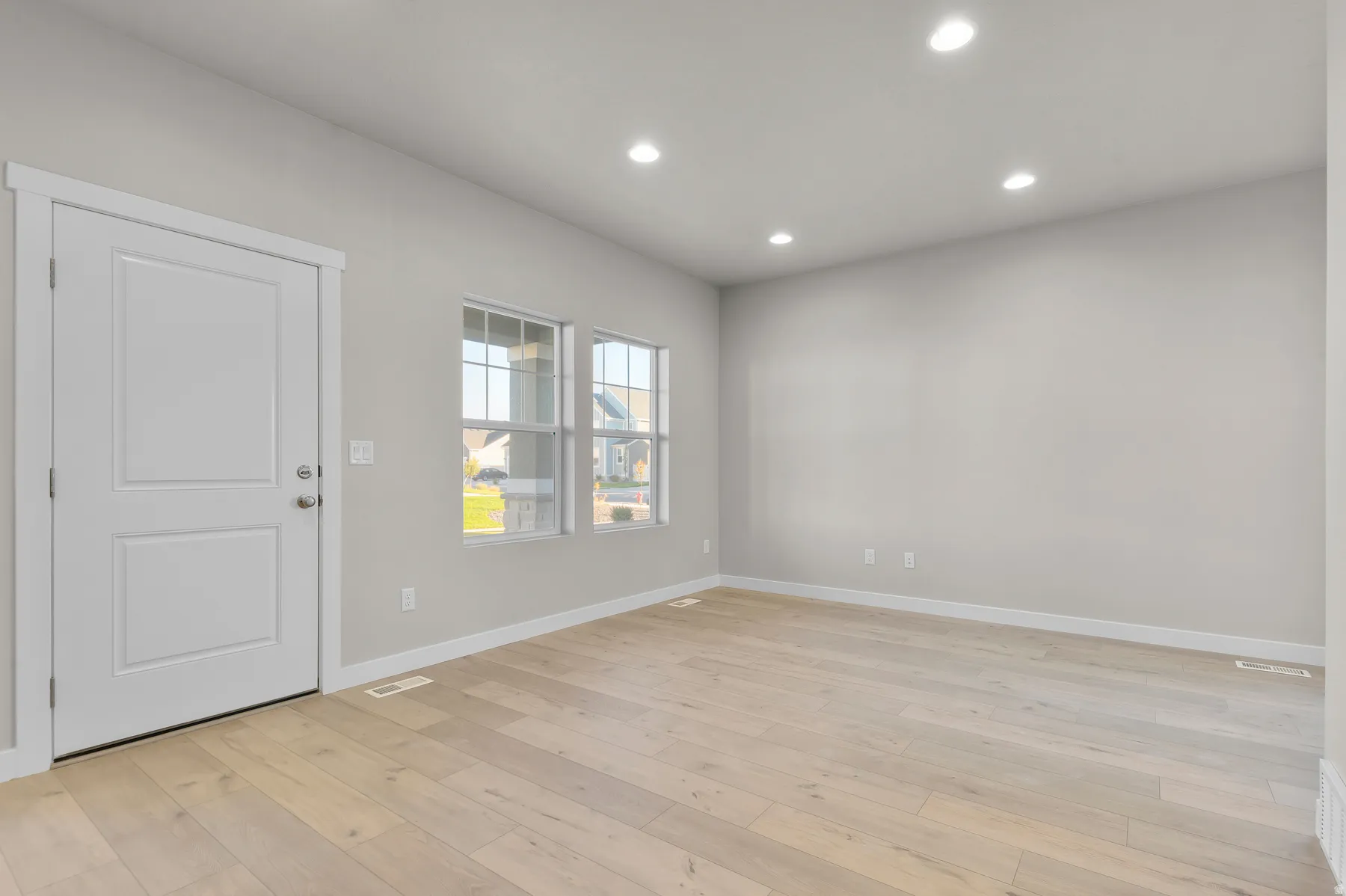 Spacious room featuring light wood-finish flooring, light gray walls, and recessed ceiling lighting