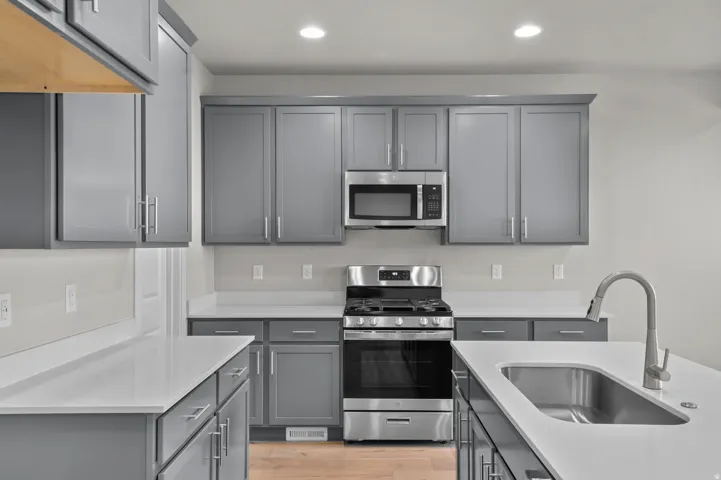 Modern kitchen featuring grey shaker-style cabinetry, white countertops, stainless steel appliances, and wood-finish flooring