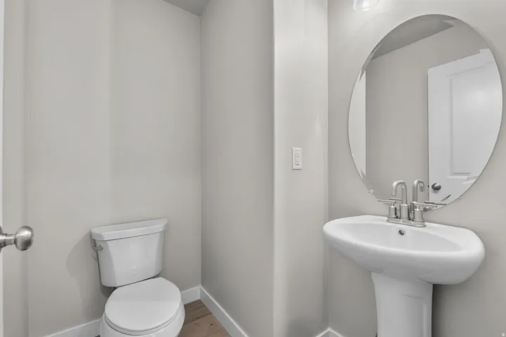 Powder room featuring a pedestal sink with a chrome faucet, an oval frameless mirror, and wood-finish flooring