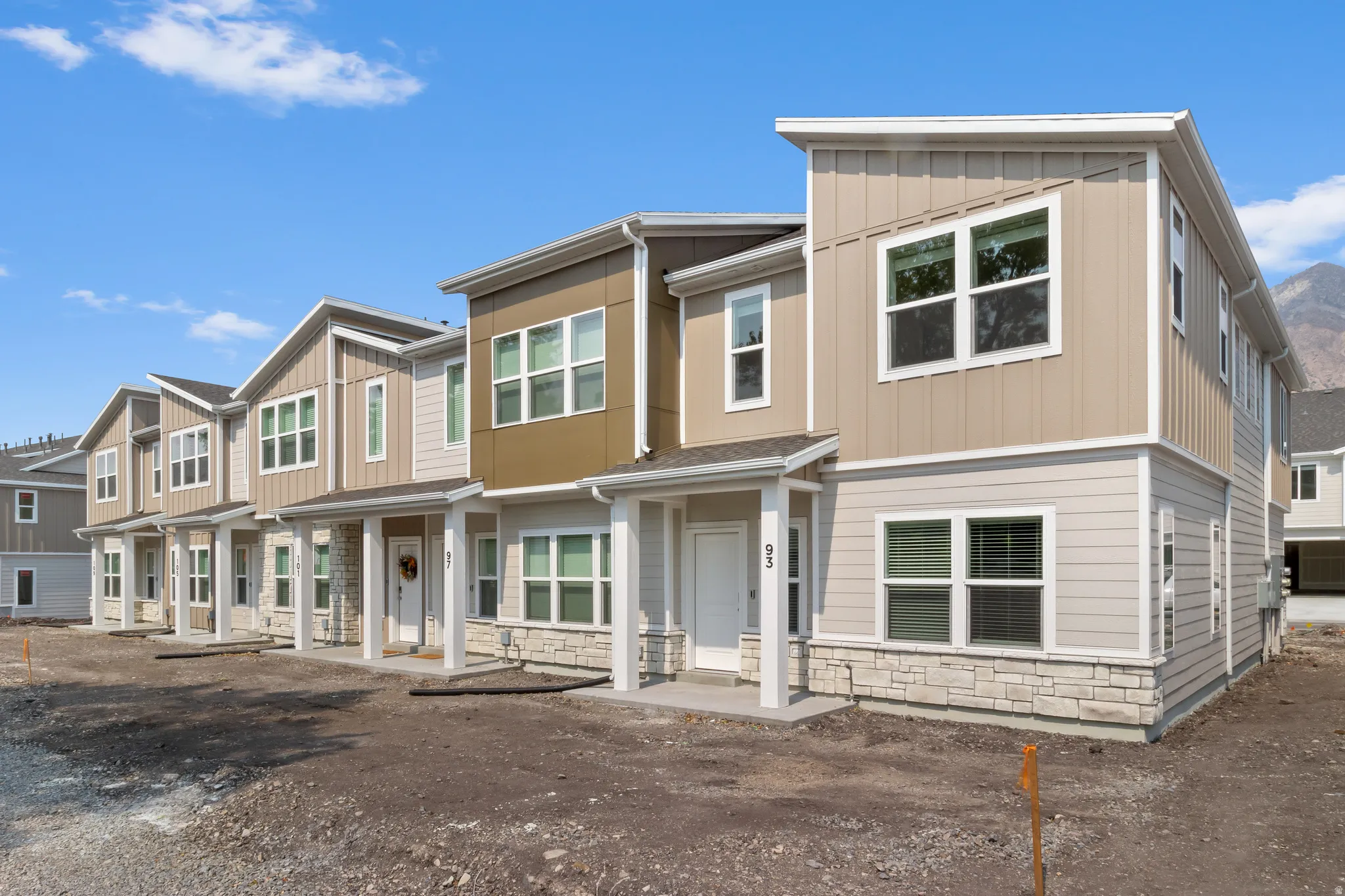 Modern townhome exterior featuring vertical and horizontal siding in neutral tones, stone veneer accents, and white trim