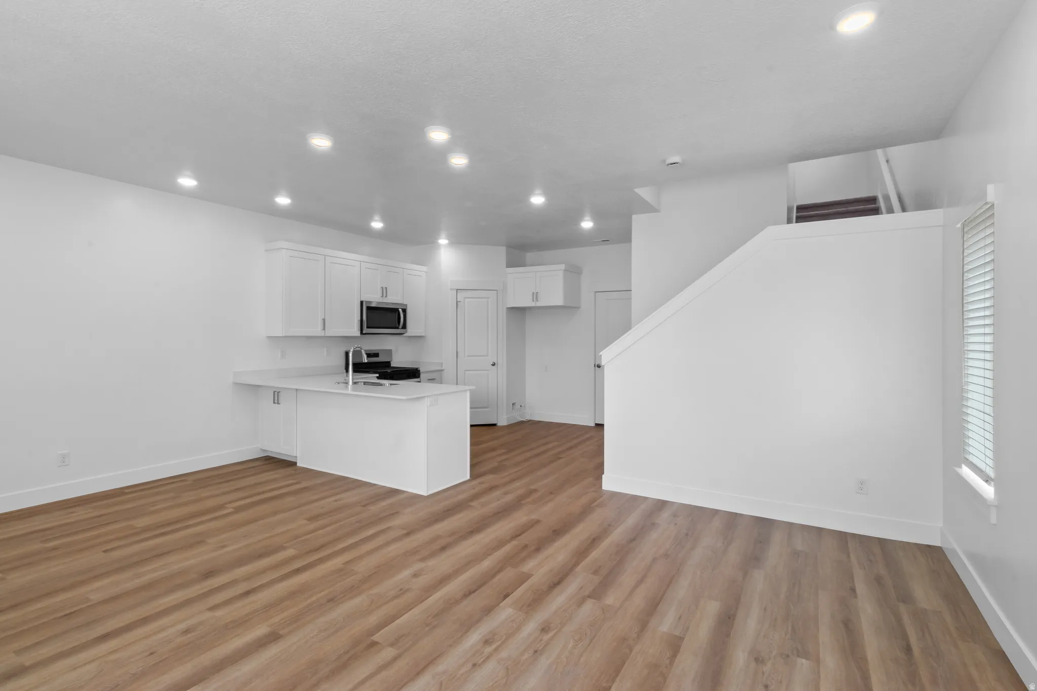 Open-concept living space featuring wood-finish flooring, recessed lighting, and a kitchen with white cabinetry and stainless steel appliances