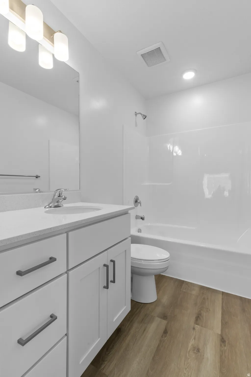 Bathroom featuring a white vanity with a light-toned countertop, a shower-tub combination, and wood-finish flooring