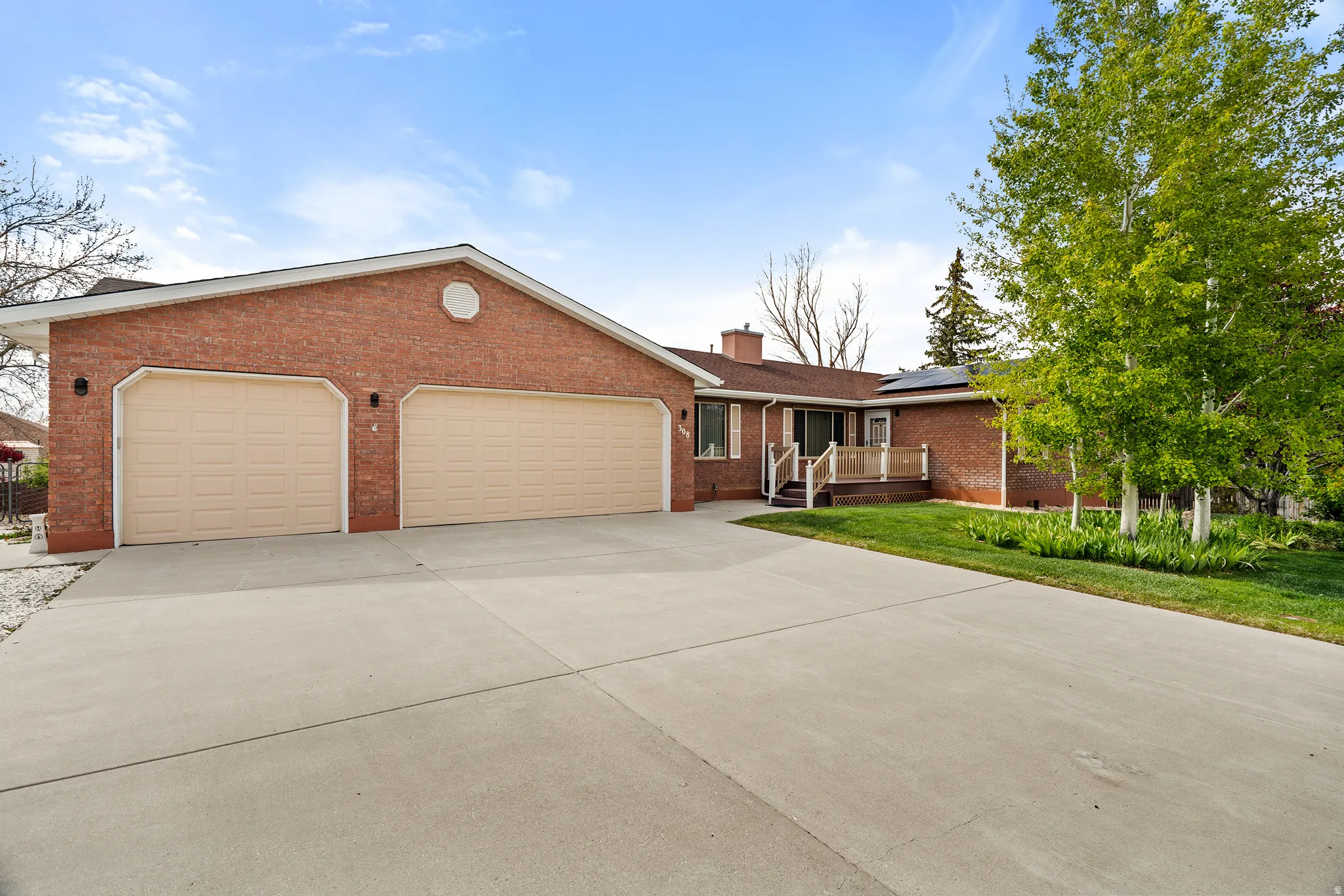 Brick-clad residence featuring a spacious concrete driveway, an integrated two-car garage with light-colored doors, a covered front porch with white railings, and mature trees enhancing the front yard landscaping