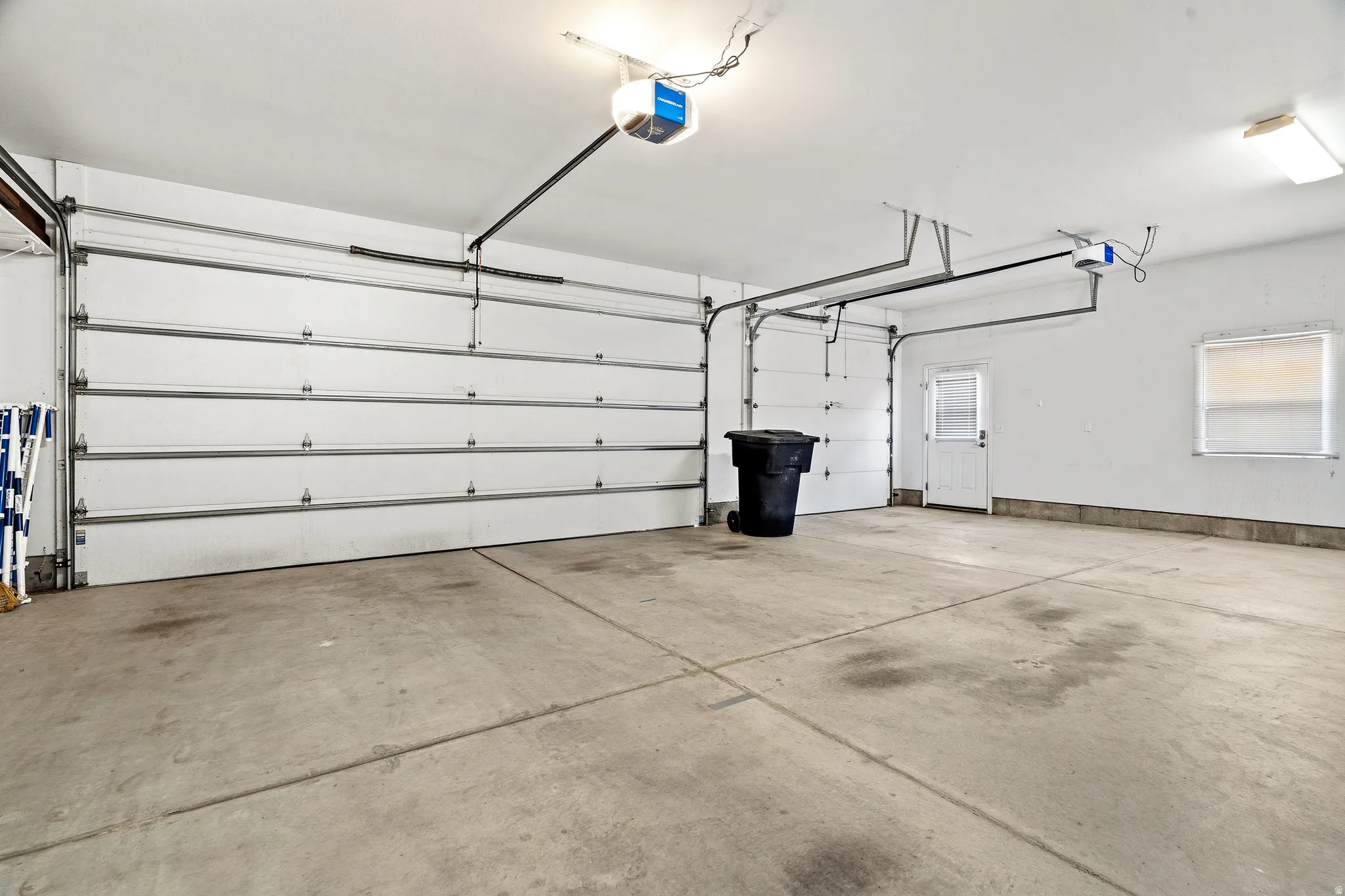 Spacious garage featuring two overhead doors, a pedestrian door, a window with blinds, and concrete flooring