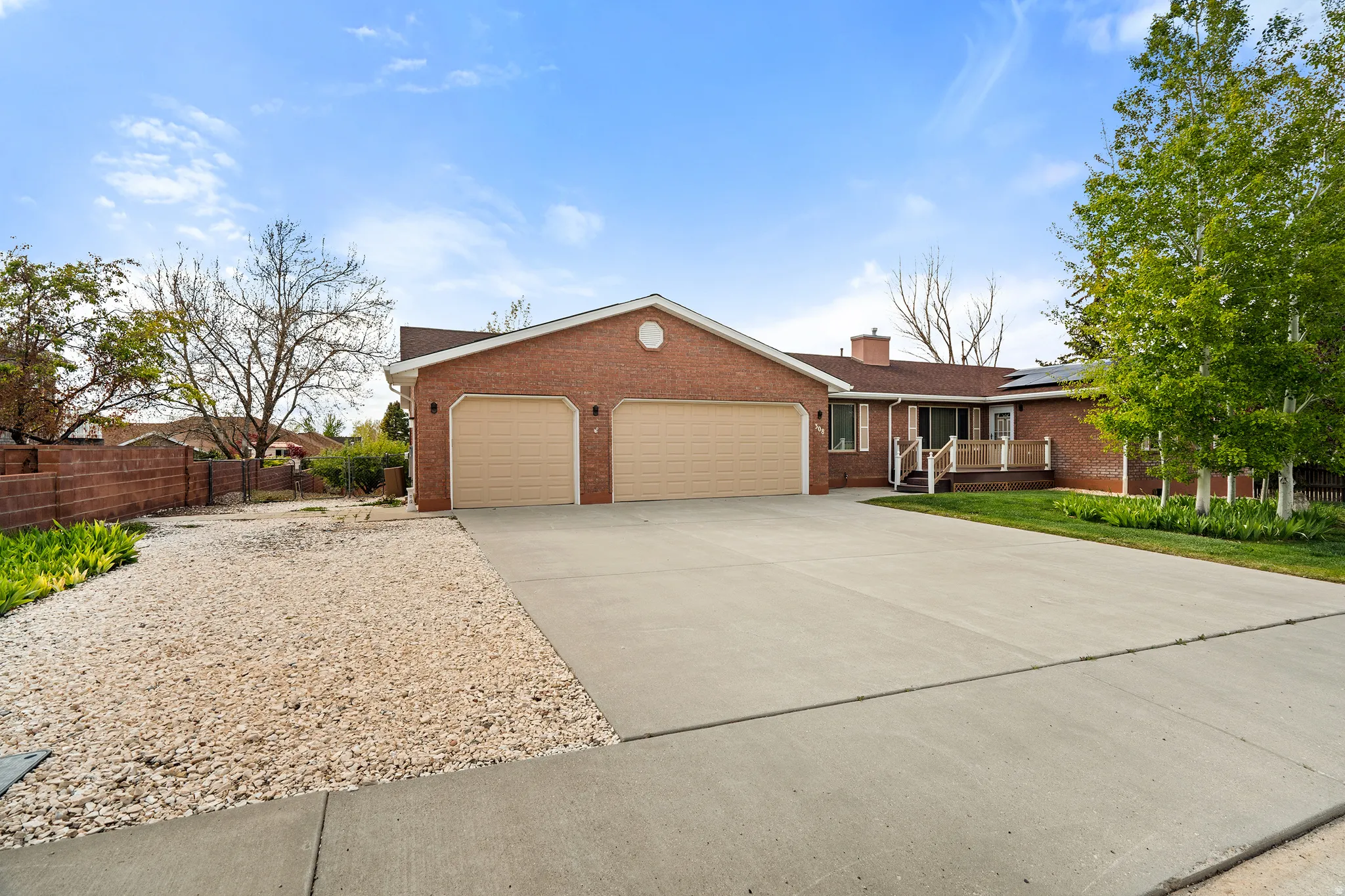 Brick exterior with a large concrete driveway, twin garage doors, a covered porch, and mature trees