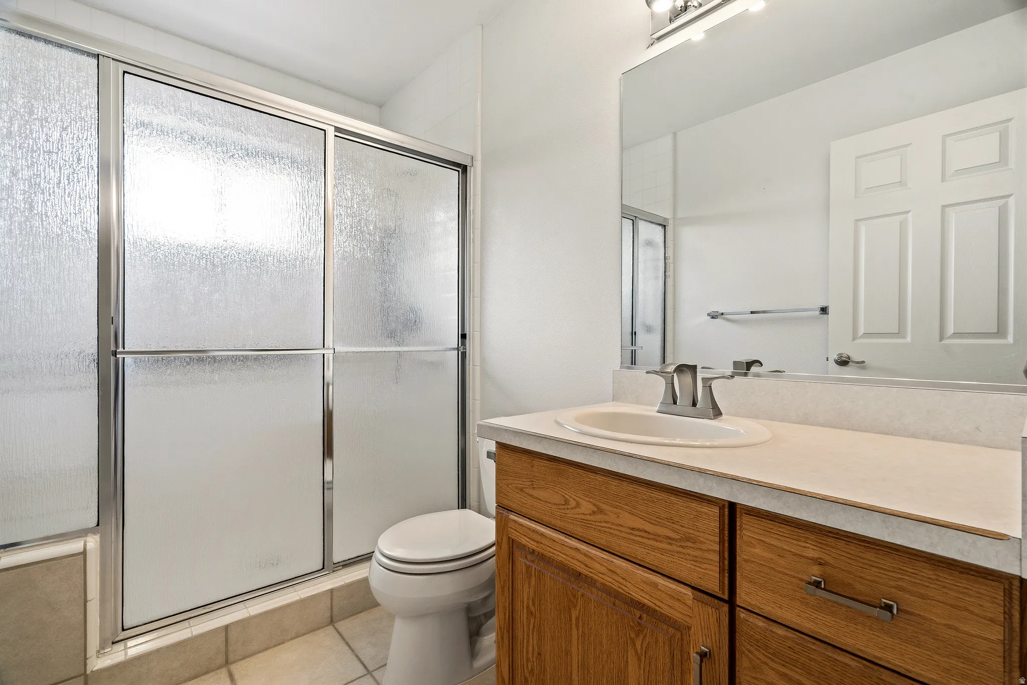 Bathroom featuring a shower/tub combination with frosted sliding glass doors, a vanity with a light-toned countertop, an integrated sink, and wood-finish cabinetry with silver-tone pulls