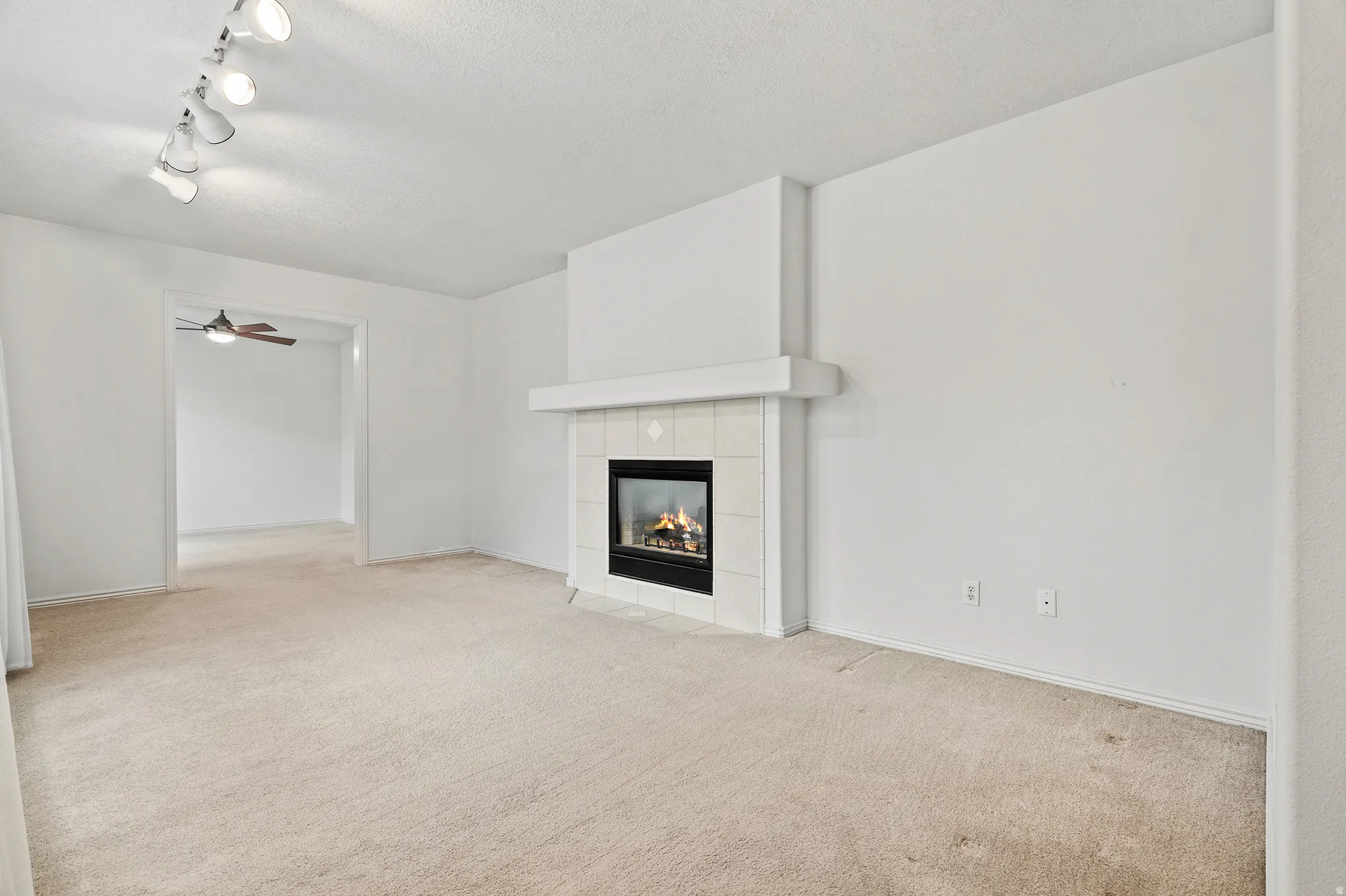 Carpeted living space featuring a fireplace with a white tile surround and a white mantel