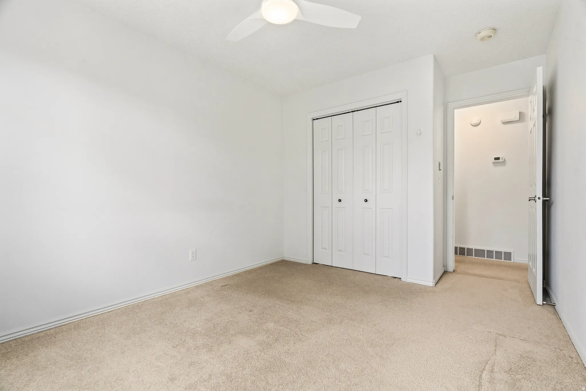 Bright room featuring plush carpet flooring, a ceiling fan, bifold closet doors with dark hardware, and a white interior door