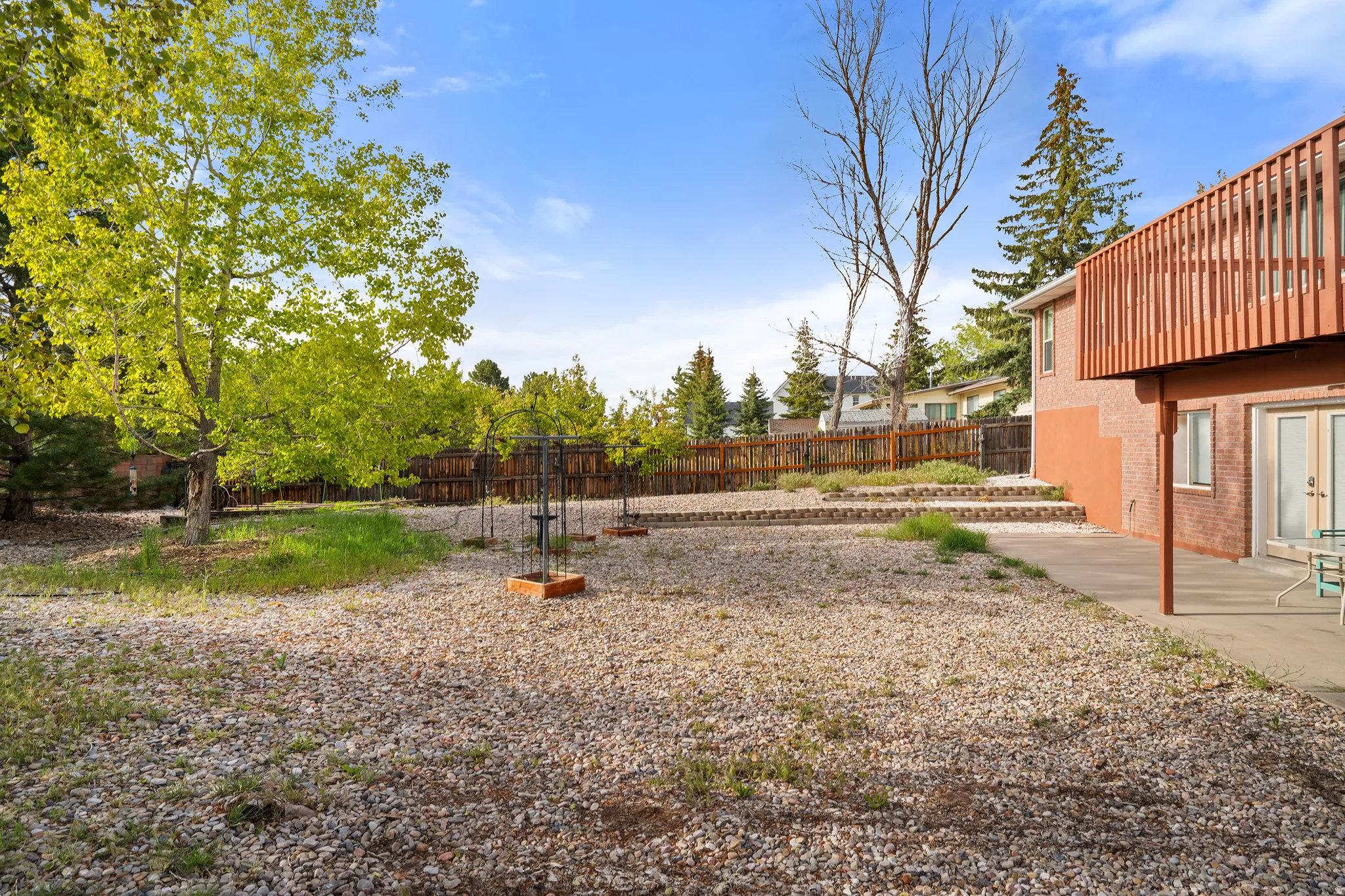 Spacious rear yard featuring a large gravel ground cover, mature deciduous trees, a privacy fence, a concrete patio, and a terraced garden area