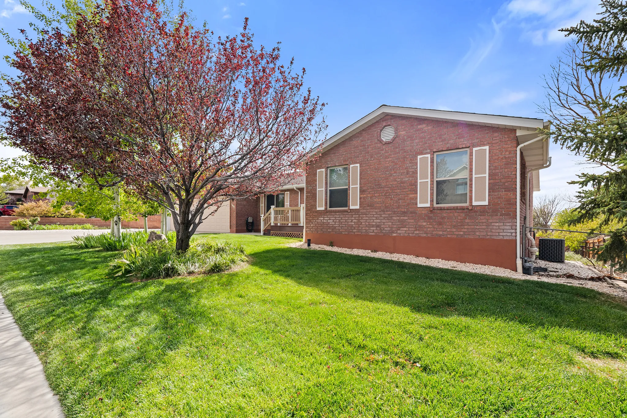 Brick exterior residence featuring a lush green lawn, mature deciduous trees, and foundation landscaping