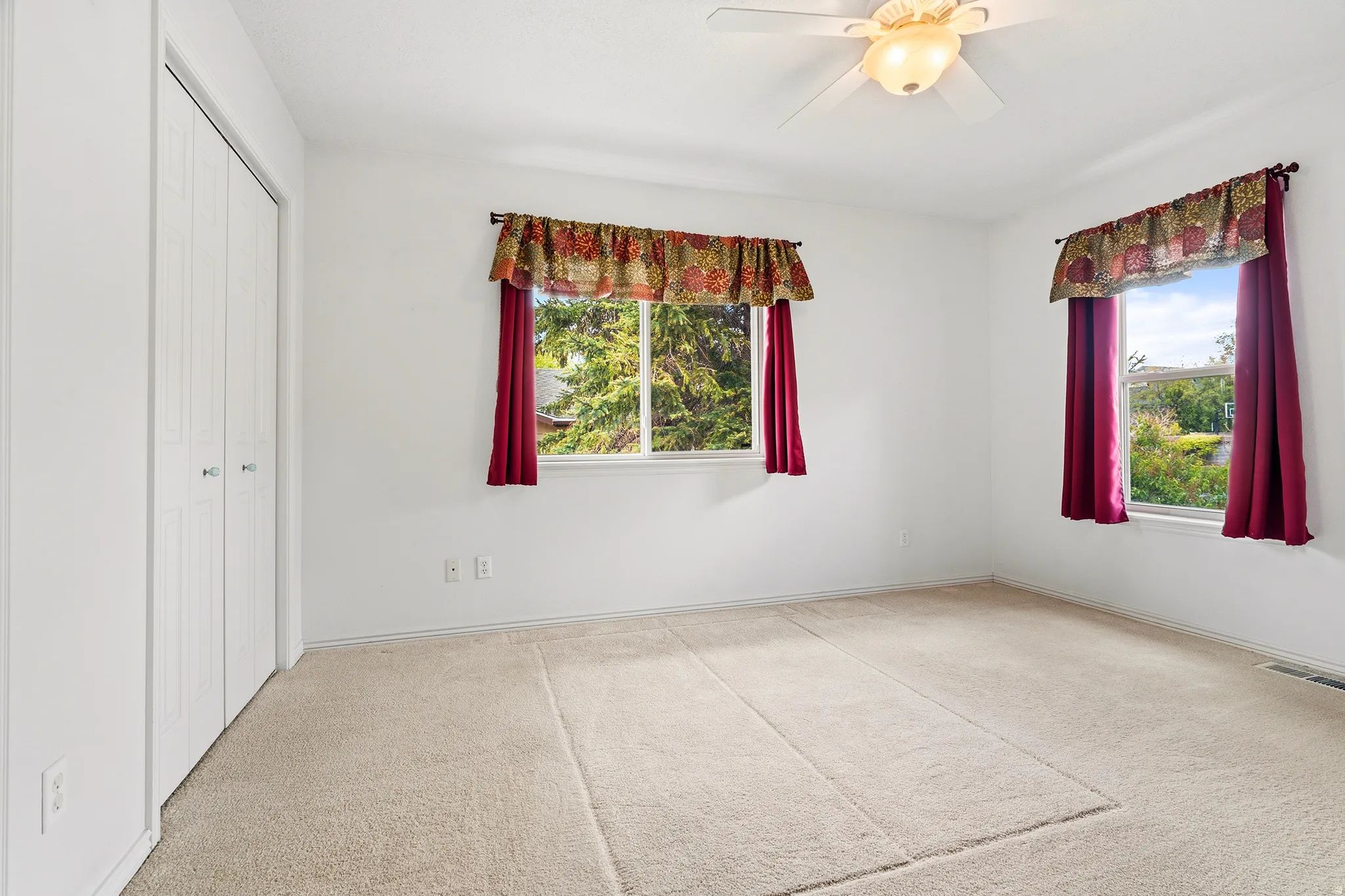 Spacious room featuring neutral carpeting, a ceiling fan with integrated lighting, and two windows offering exterior scenery