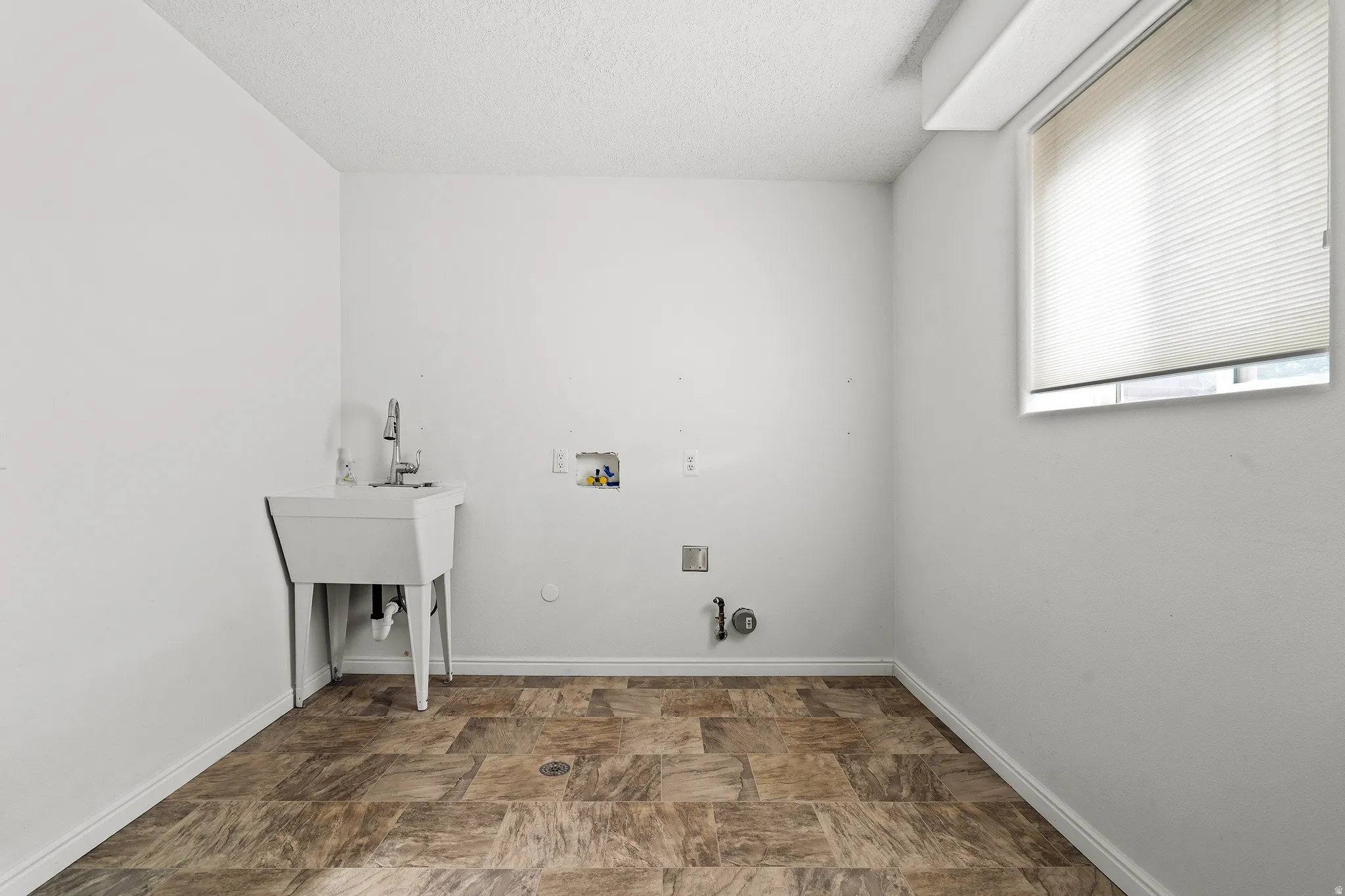 Laundry area featuring a utility sink with faucet, window with blinds, and durable vinyl flooring