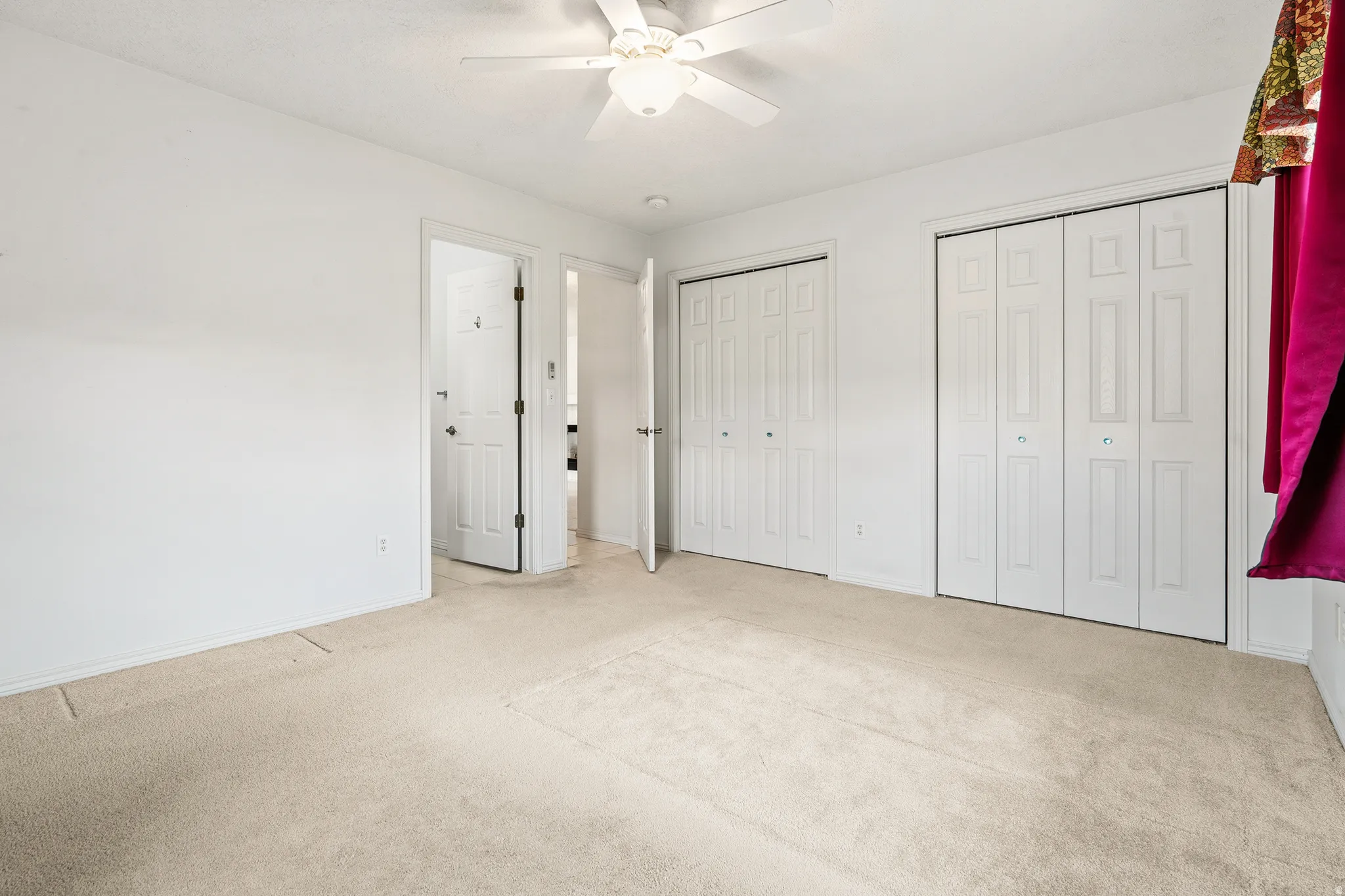 Bedroom featuring light-toned carpet flooring, white walls, two bi-fold closet doors, and a ceiling fan with integrated lighting