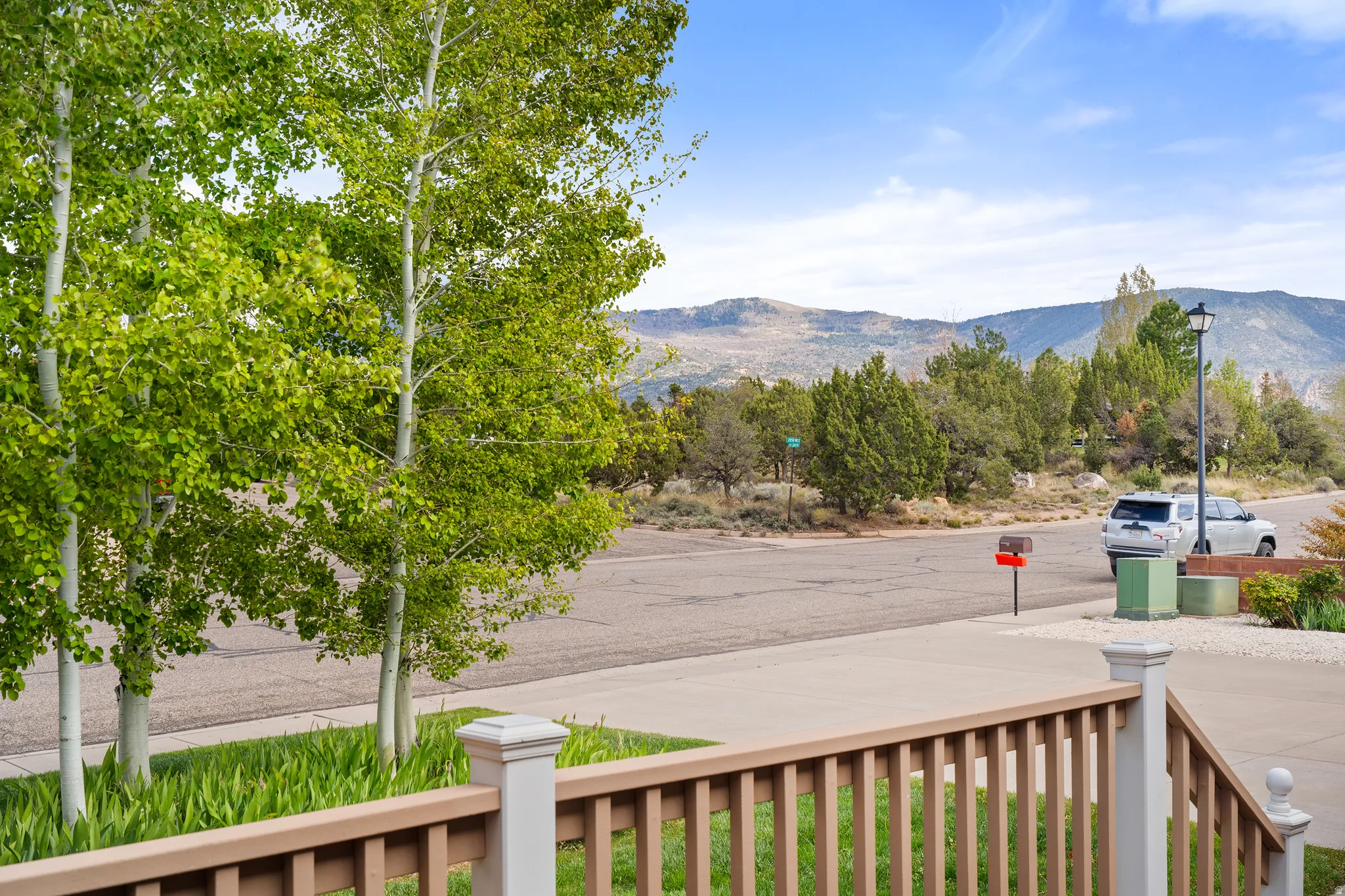 Front porch railing with a mountain backdrop, mature trees, and paved street