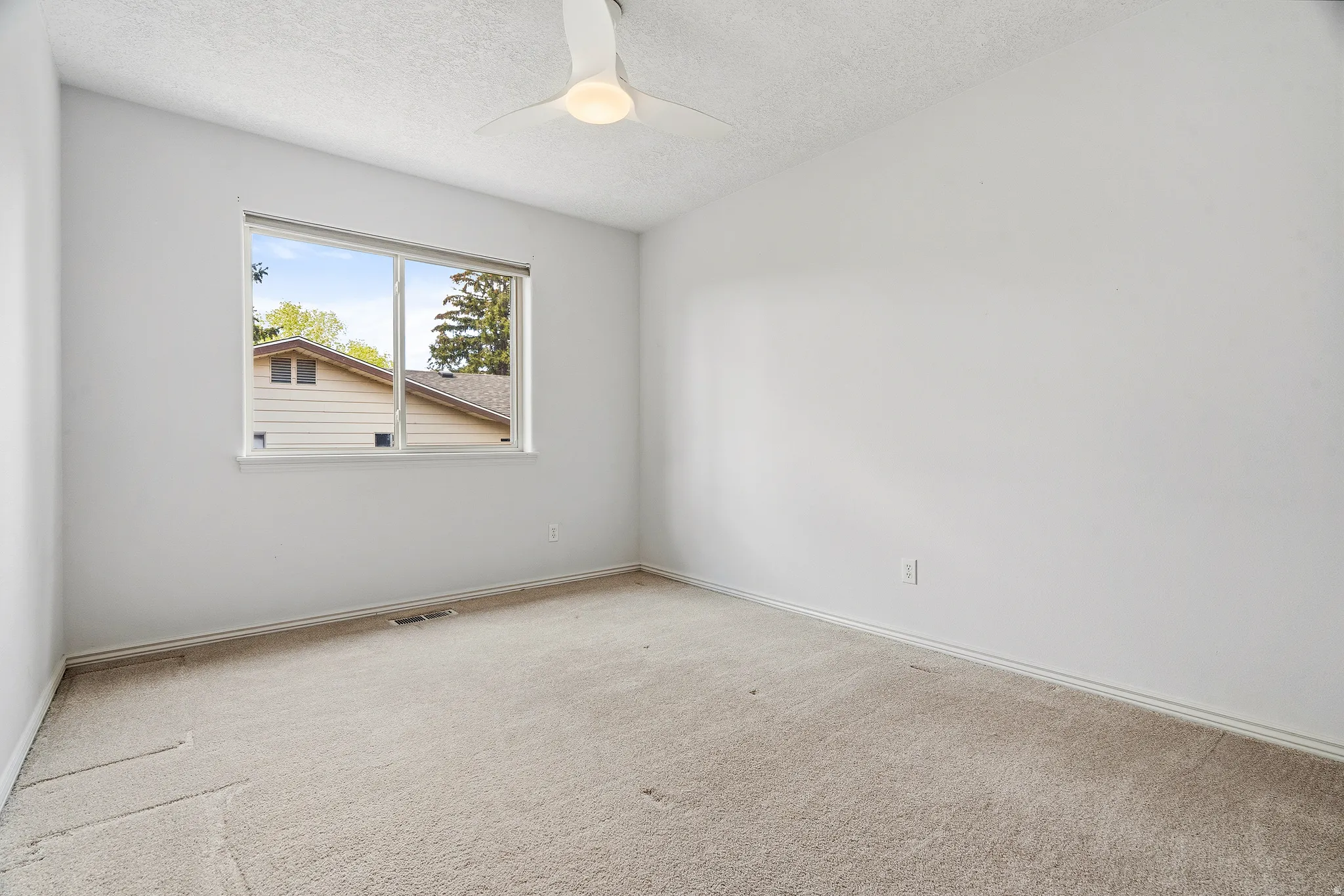 Carpeted room with a large window and a ceiling fan