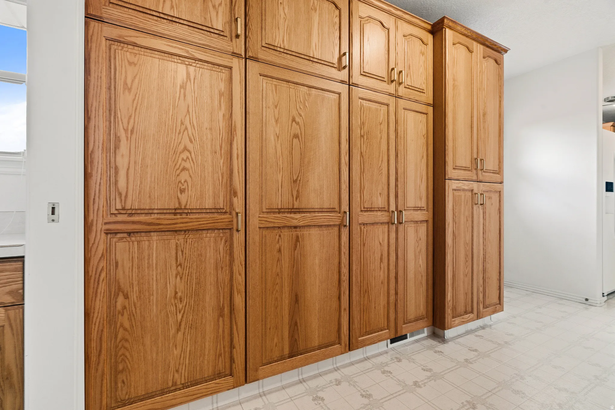 Extensive wood-finish cabinetry offering abundant storage, featuring panel door fronts with decorative trim, brass hardware, and a light-toned patterned floor