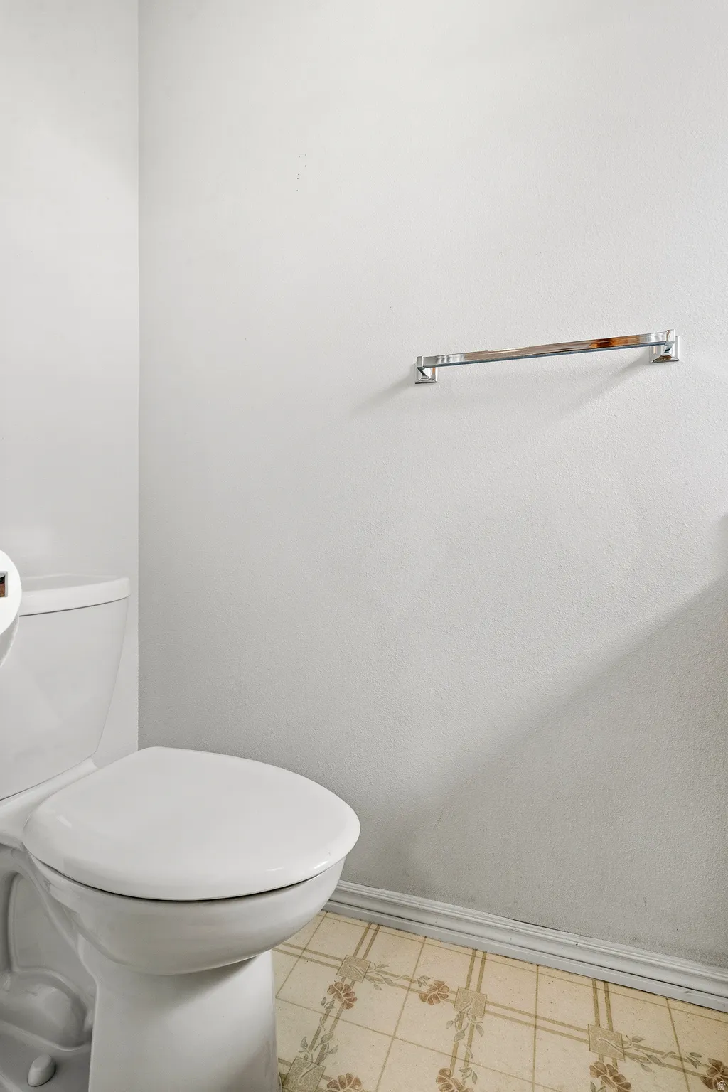 White toilet with a round bowl, chrome towel bar, and patterned floor tile