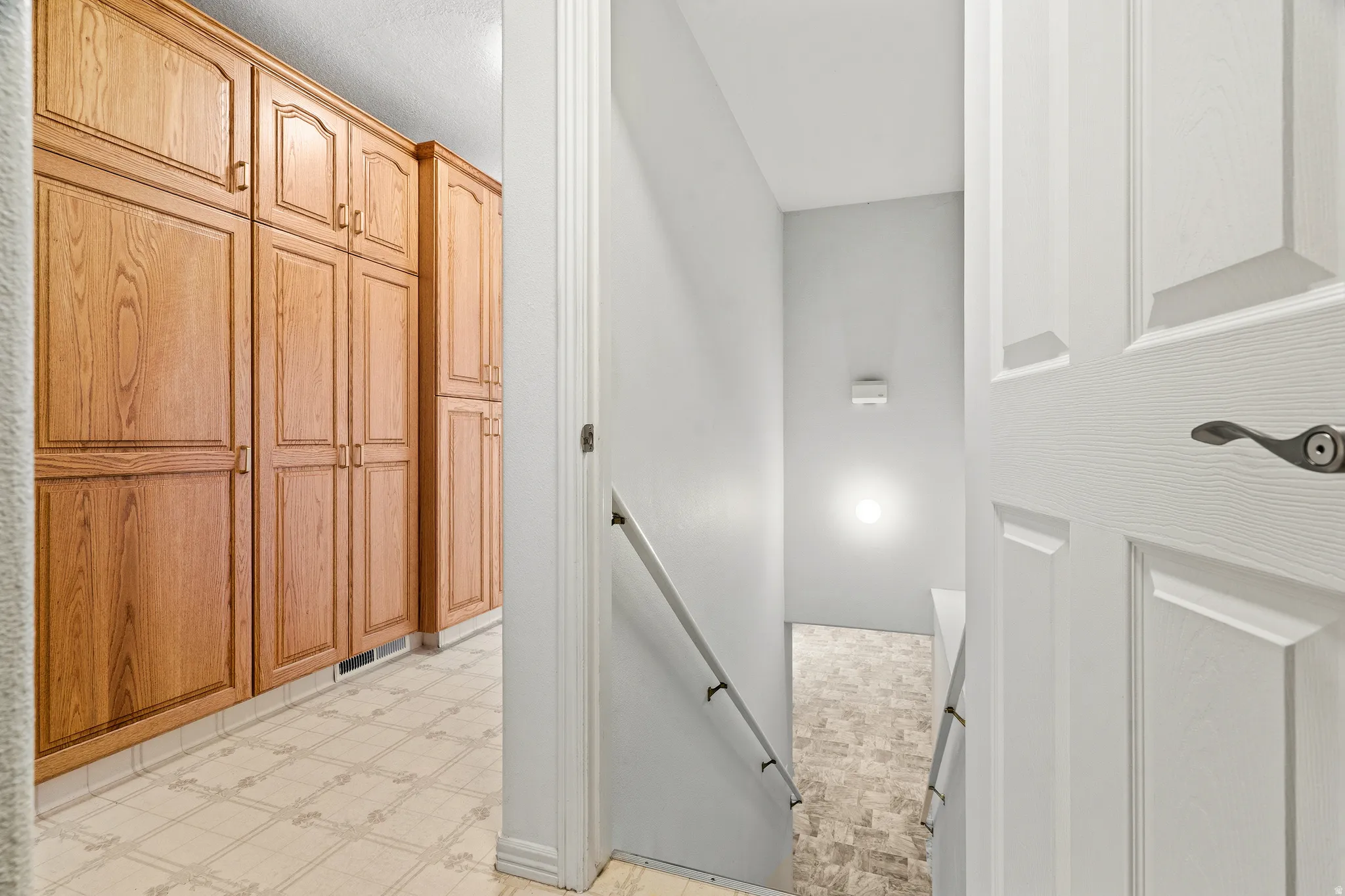 Hallway featuring extensive wood-finish cabinetry with arched panel doors, patterned flooring, and a white paneled door
