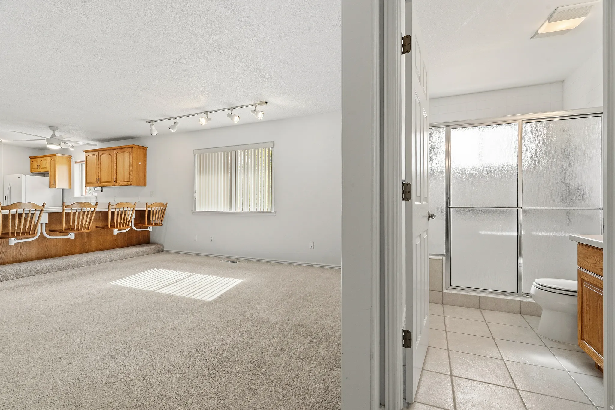 Kitchenette and bathroom combination featuring a bar-height counter with built-in seating, light wood cabinetry, white appliances, and track lighting