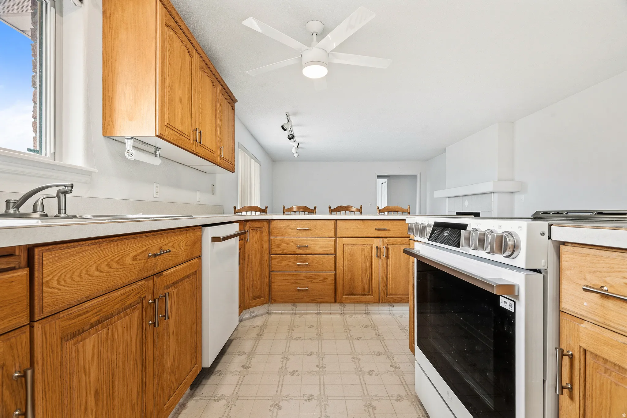 Kitchen featuring wood cabinetry, light-toned countertops, a built-in dishwasher, and a white freestanding range