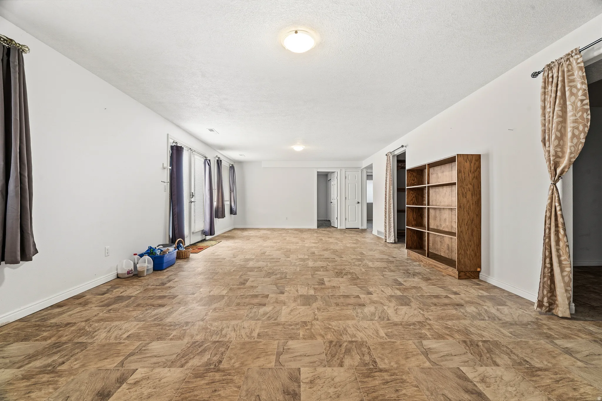 Expansive open-concept room featuring light-toned interior walls, a neutral-toned tile-patterned flooring, and multiple overhead light fixtures