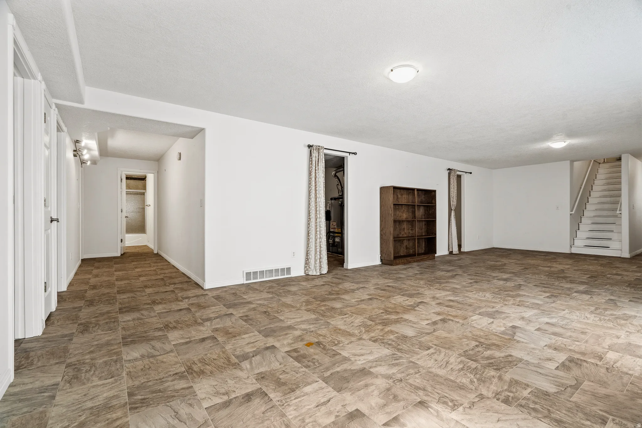 Spacious lower-level area featuring neutral walls, patterned tile flooring, recessed lighting, and a white staircase with a matching handrail