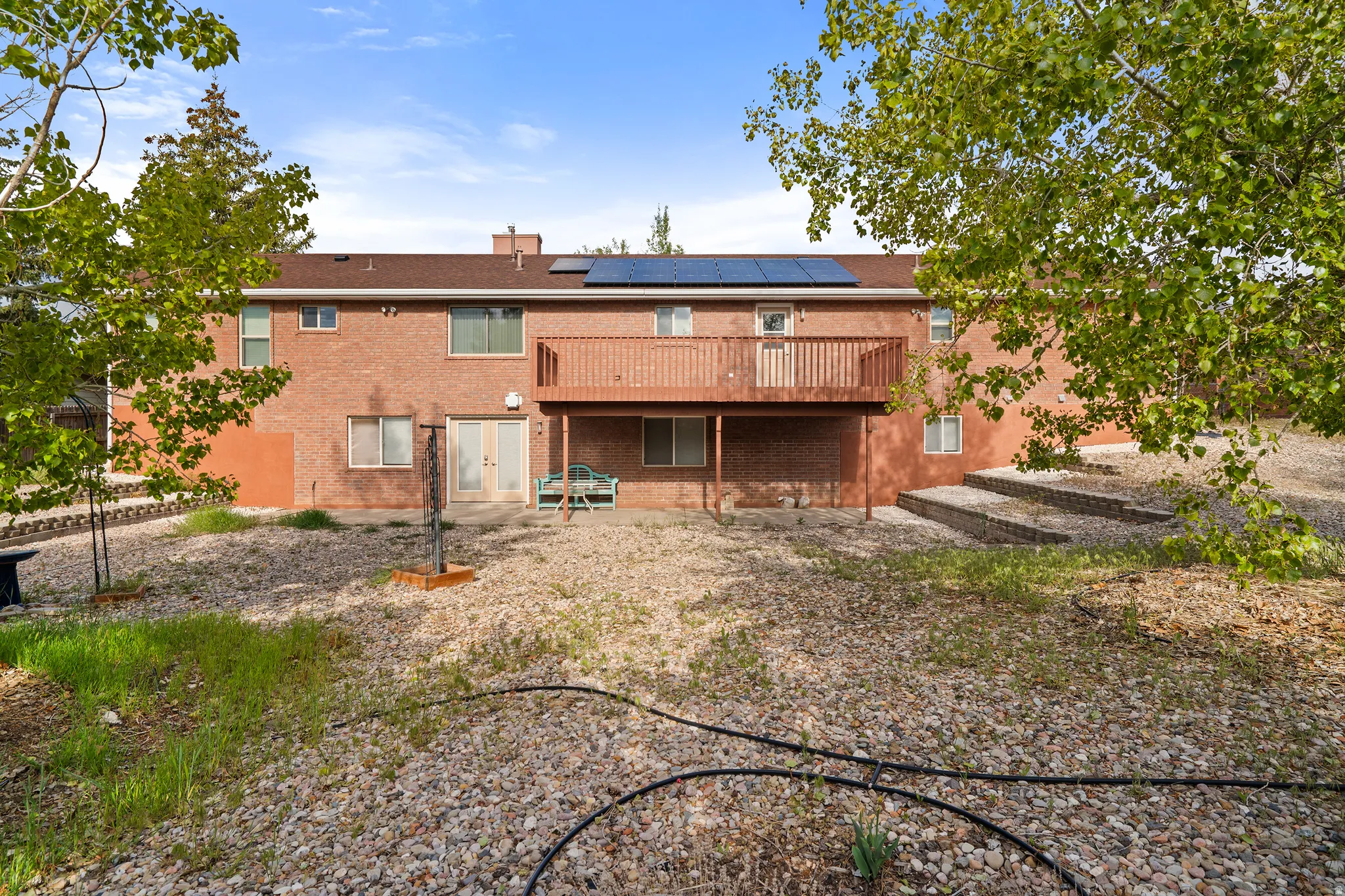 Brick exterior featuring a second-story wooden deck, ground-level patio doors, and solar panels