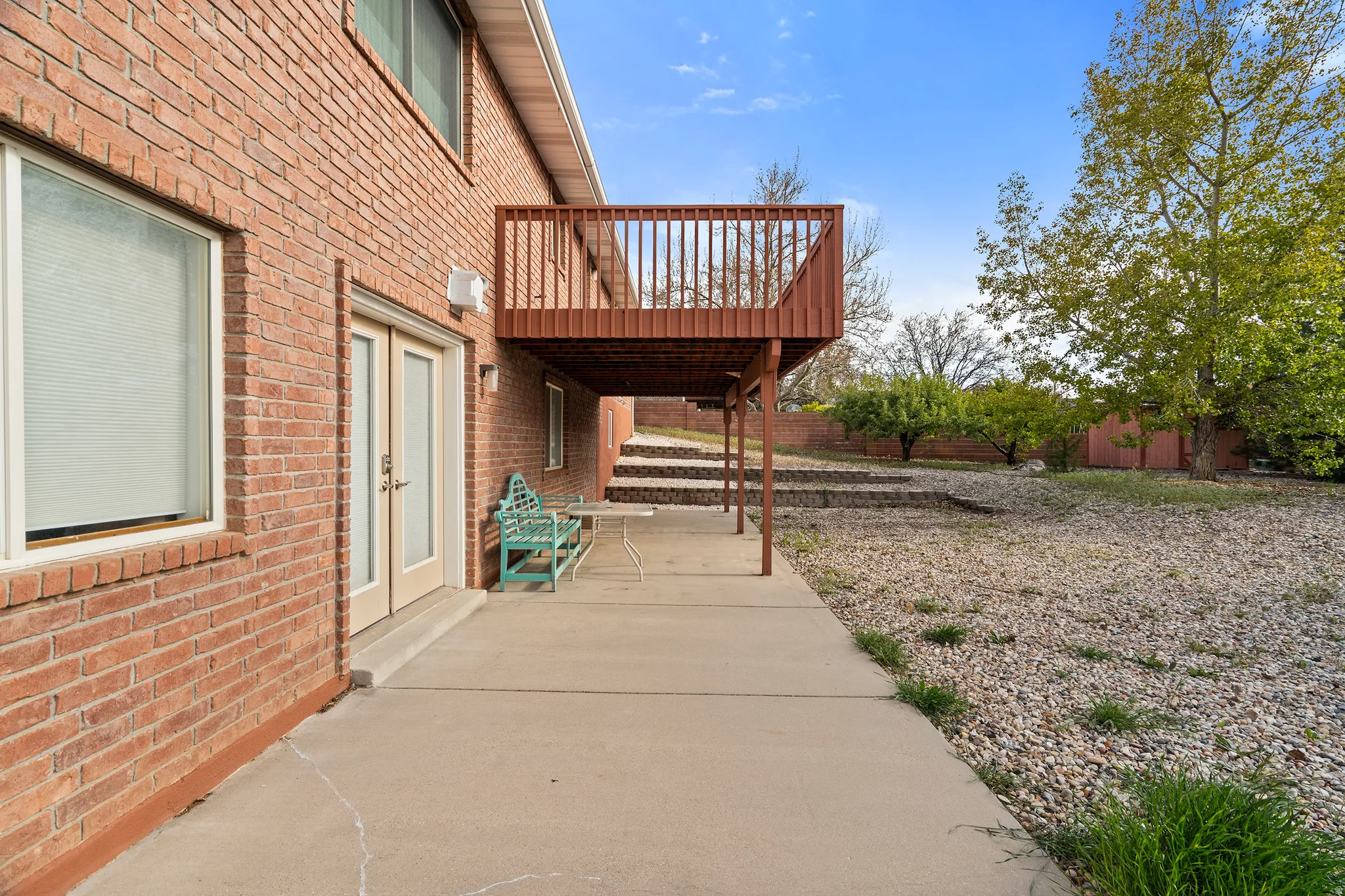 Brick exterior featuring a private upper-level deck, concrete patio, and French doors