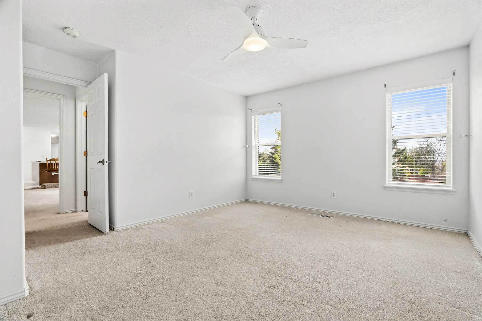 Spacious room featuring carpeted flooring, a ceiling fan with integrated lighting, and two windows with blinds