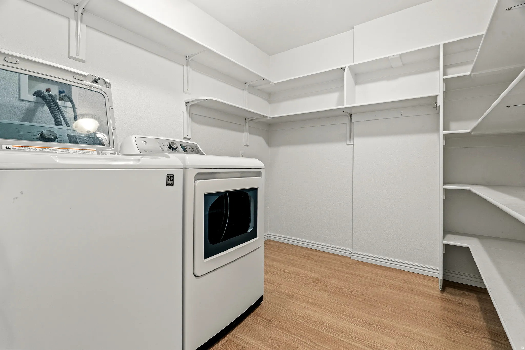 Dedicated laundry area featuring wood-finish flooring, white walls, and built-in white shelving