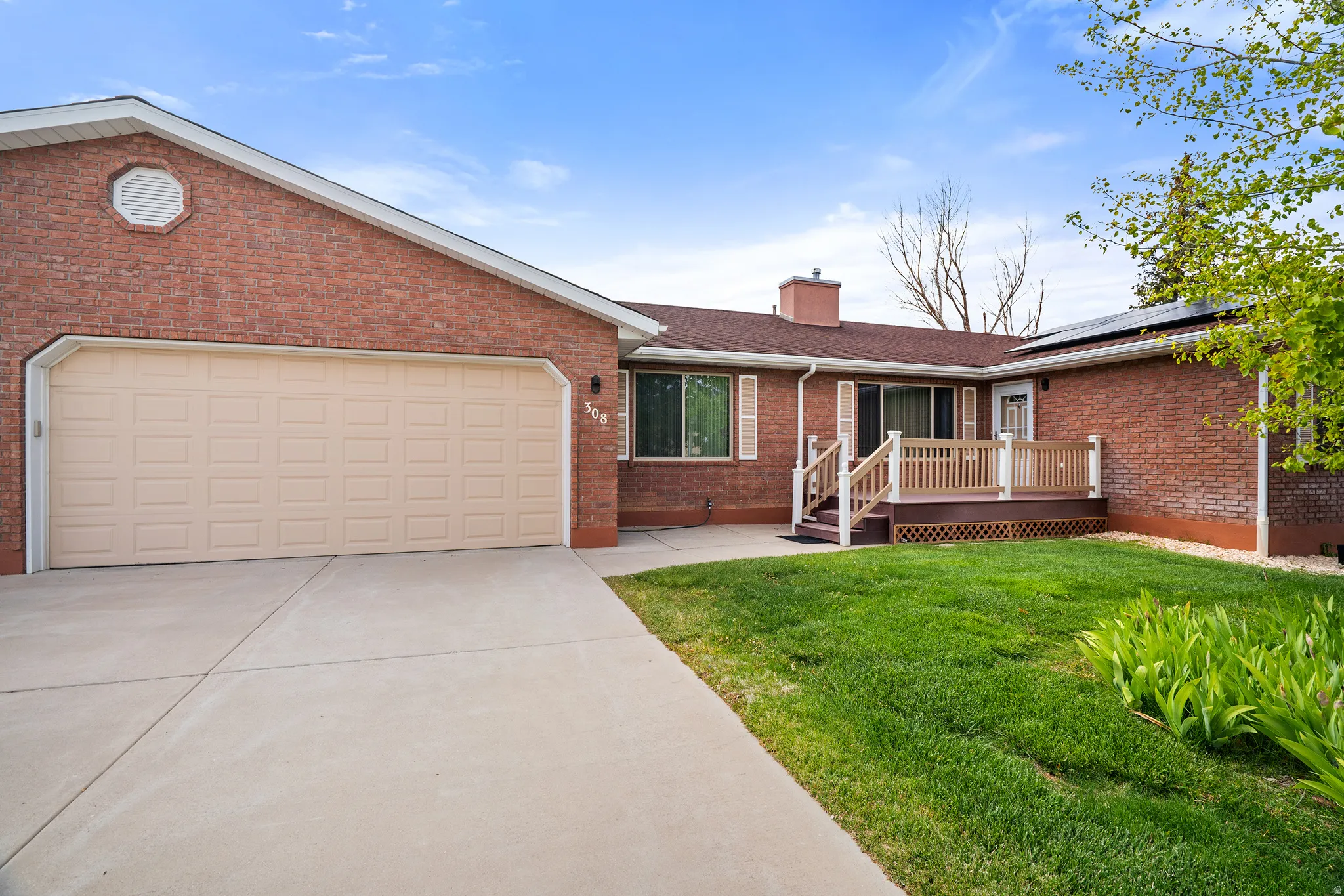 Brick exterior featuring a two-car garage, extended driveway, and a front deck with railings