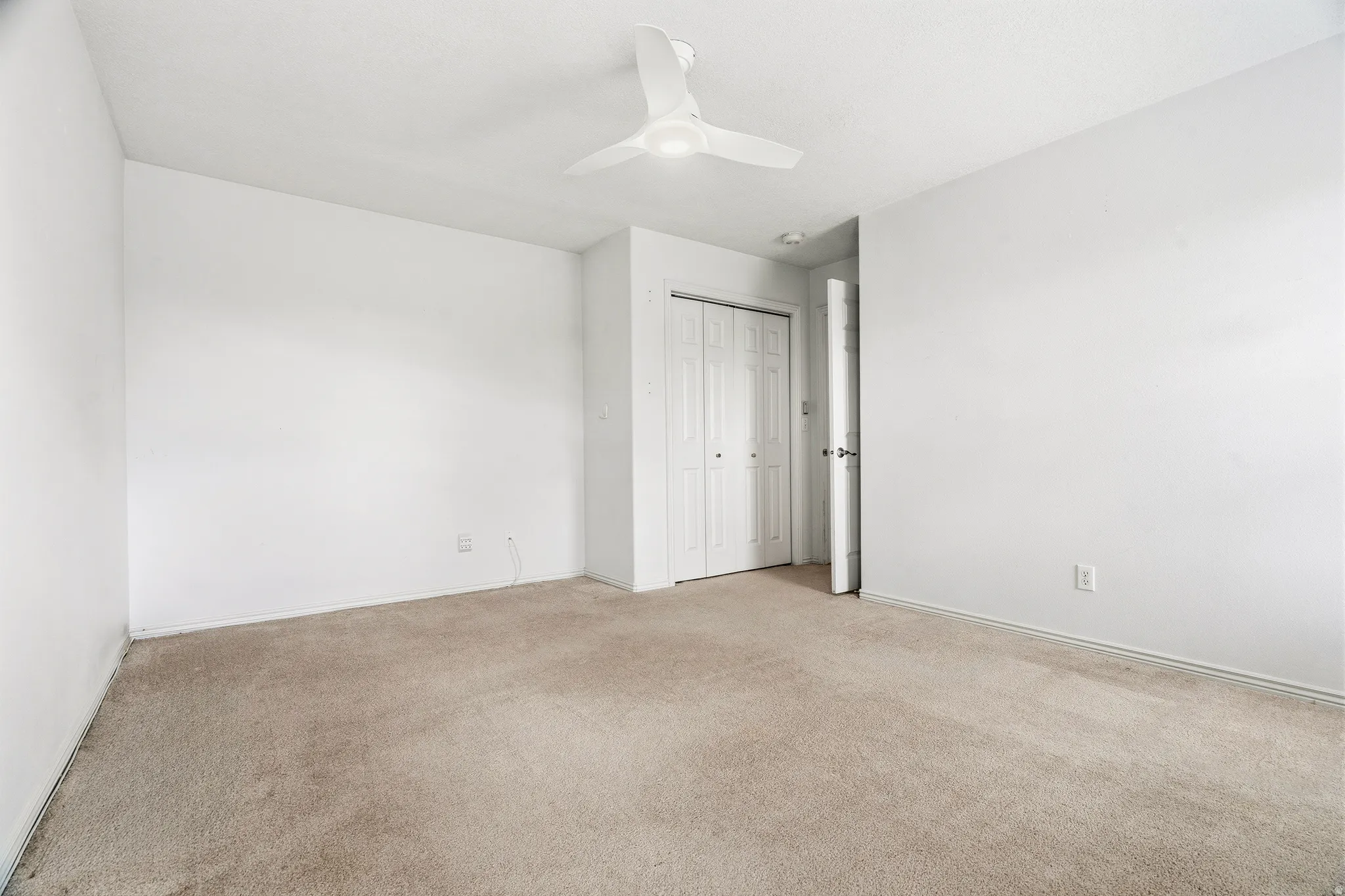 Carpeted room with white walls, a ceiling fan, and a bi-fold closet door