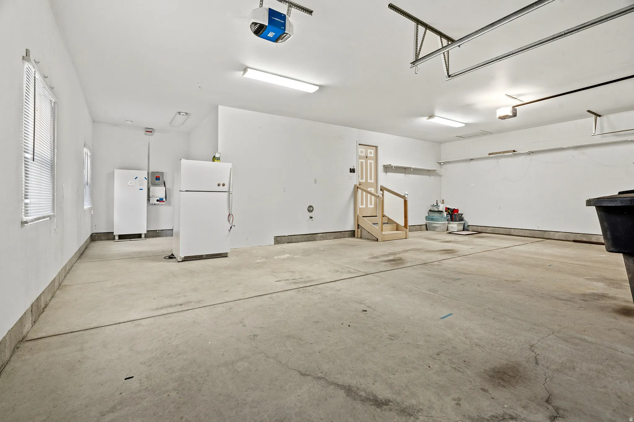 Spacious garage featuring a concrete floor, white painted walls, multiple fluorescent light fixtures, and a garage door opener system