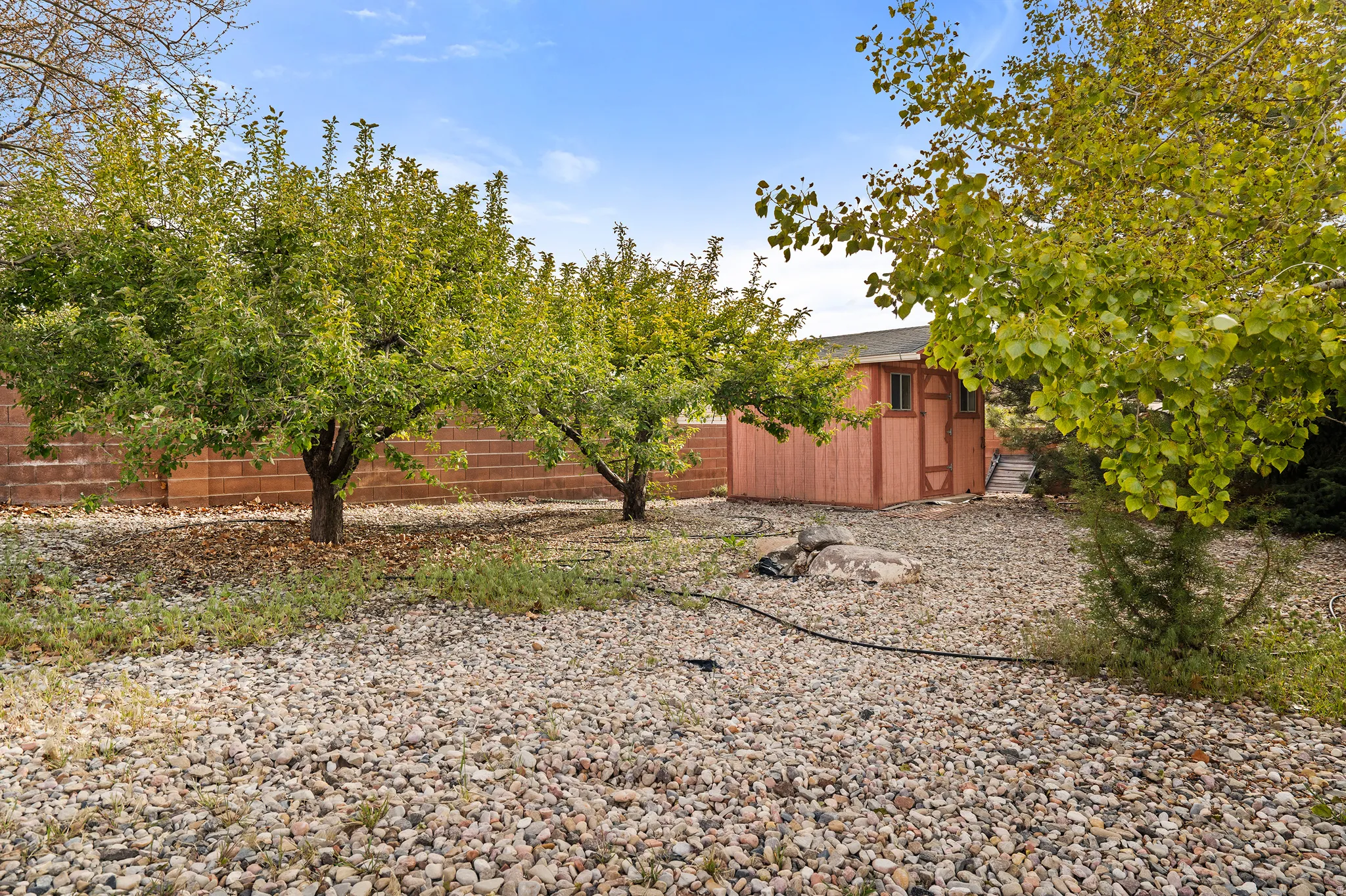 Expansive backyard featuring a gravel ground cover, mature trees, a stained wood storage shed with a shingled roof, and a terraced retaining wall