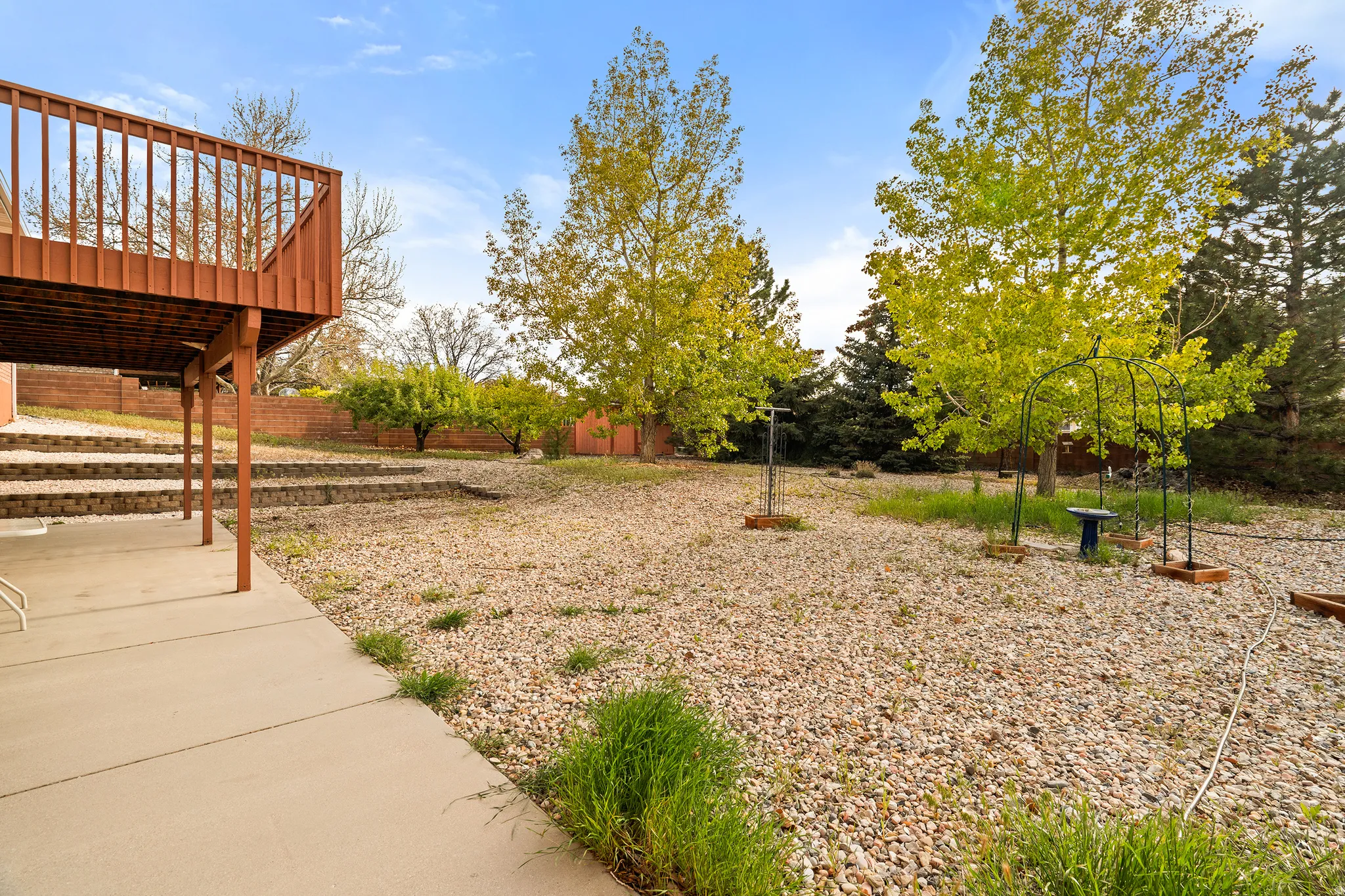Spacious backyard featuring a multi-level deck with wood railing, concrete patio, and terraced retaining walls