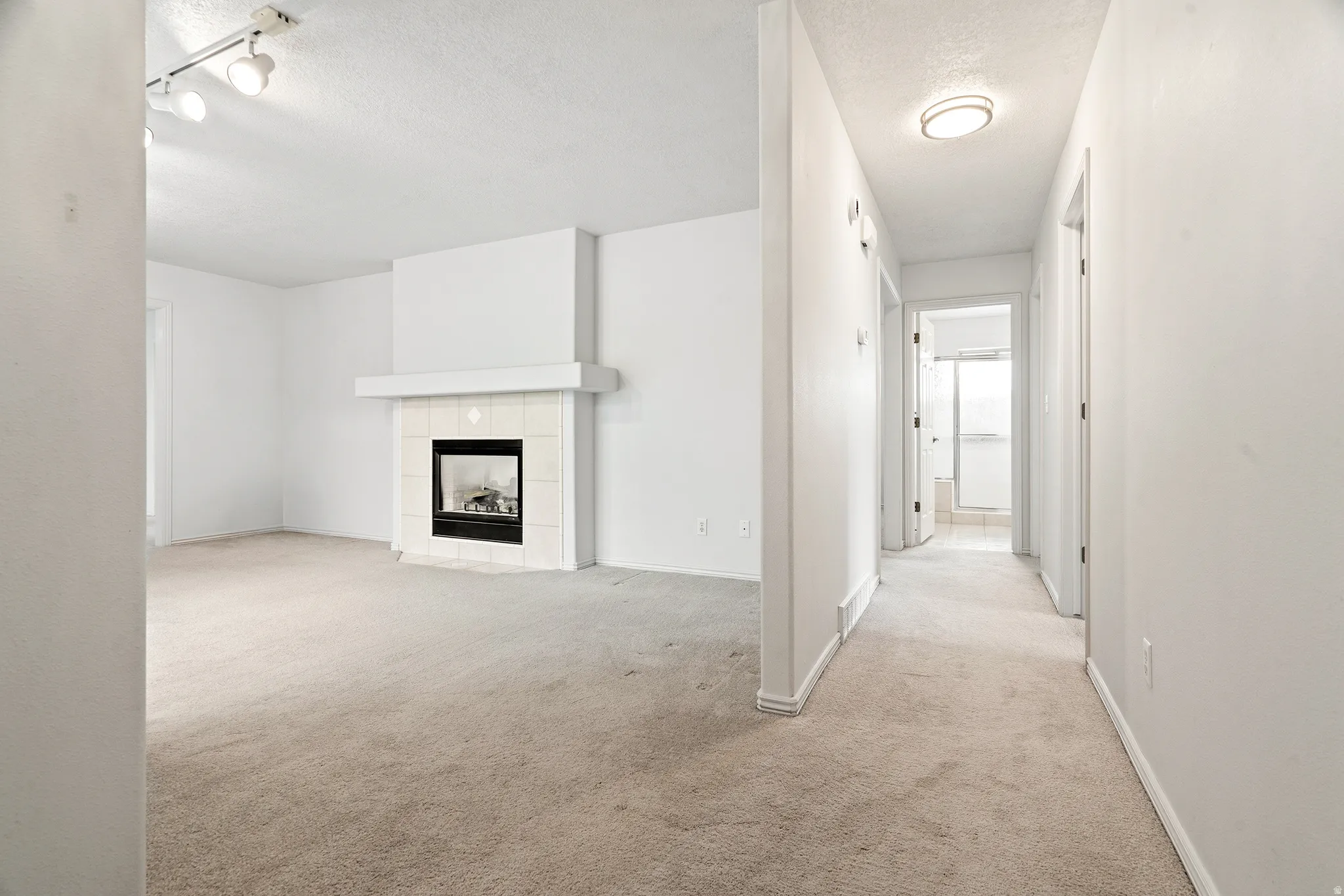 Living area featuring a fireplace with a light-toned tile surround and hearth, track lighting, and neutral carpeting
