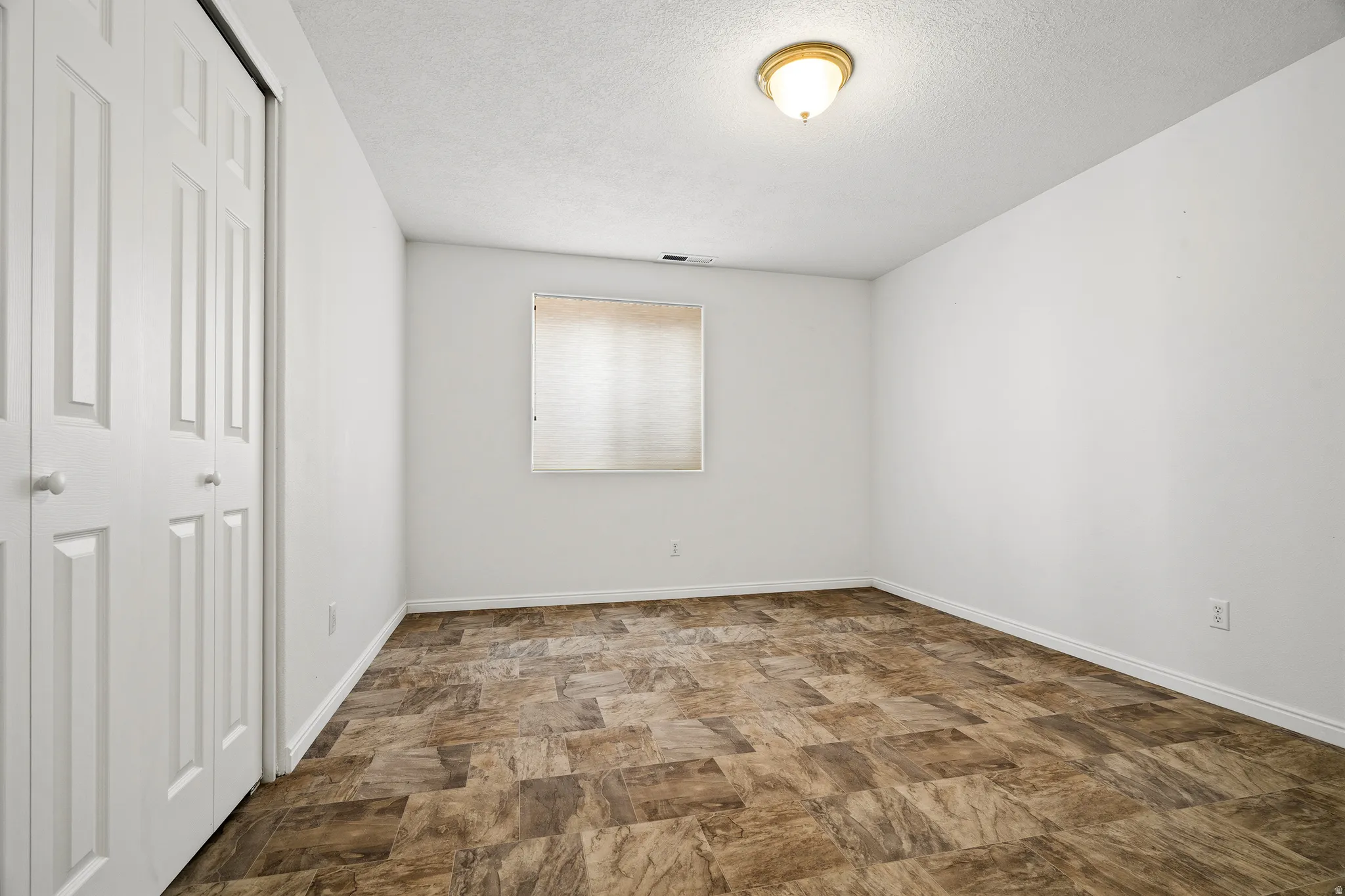 Neutral interior space featuring durable patterned flooring, a window with horizontal blinds, and a bi-fold closet with panel doors