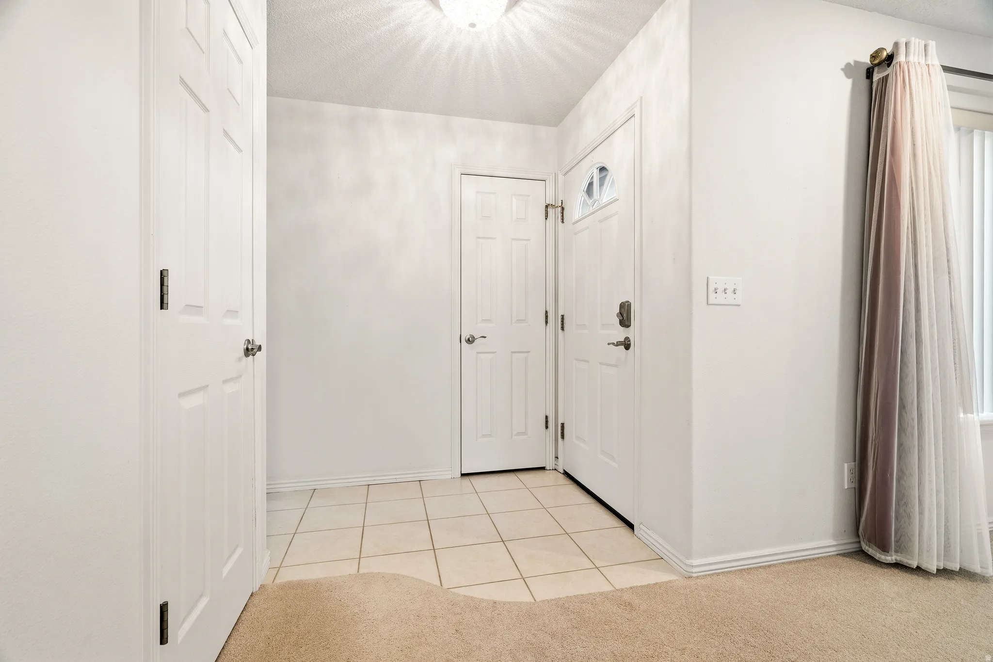 Entryway featuring ceramic tile flooring, a white paneled door with decorative glass, and a large window with vertical blinds
