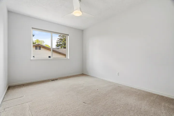 Carpeted room with a large window and a ceiling fan