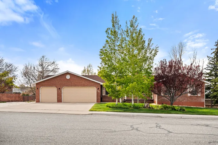 Brick exterior residence with a two-car garage, mature trees, and a concrete driveway