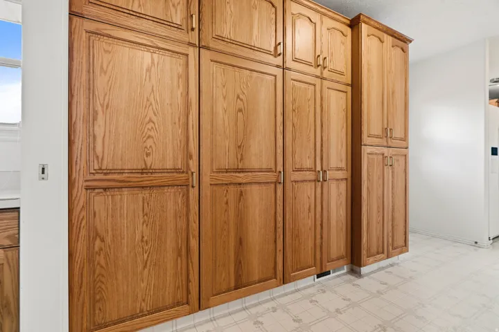 Extensive wood-finish cabinetry offering abundant storage, featuring panel door fronts with decorative trim, brass hardware, and a light-toned patterned floor
