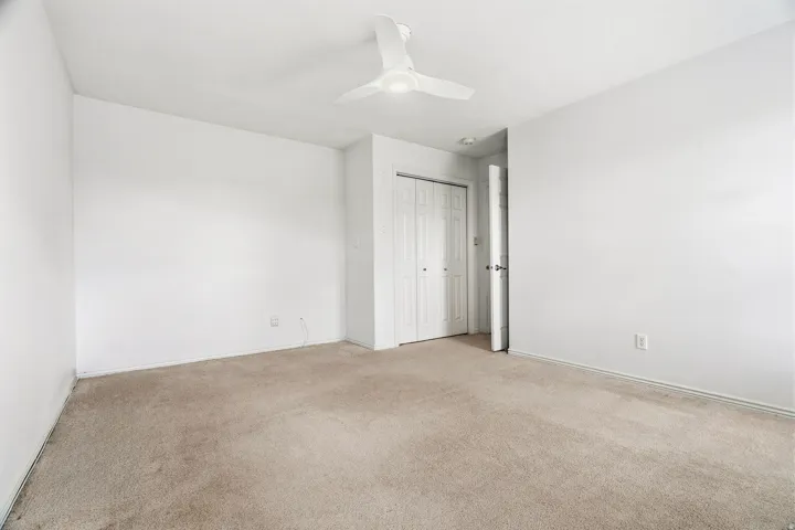 Carpeted room with white walls, a ceiling fan, and a bi-fold closet door