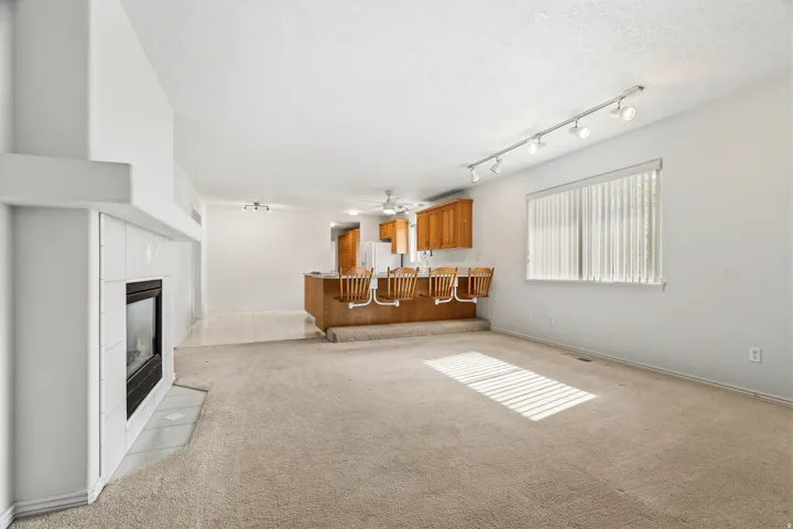 Spacious living area featuring a central fireplace with a tile surround, light-toned carpeting, and a large window with horizontal blinds
